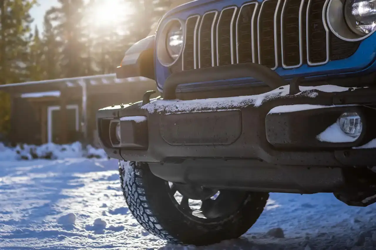 Jeep 2025 Jeep Wrangler 4xe Backcountry in profile view, showing black exterior decals, 20-inch wheels with all-terrain tires, steel bumpers, and rock rails against a natural outdoor background. (image 3 of 11)