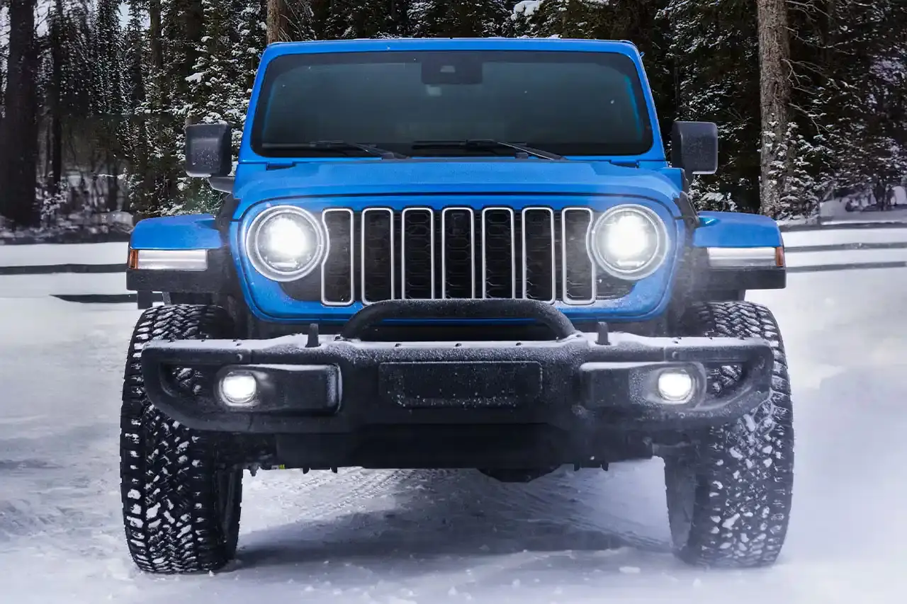 Jeep 2025 Jeep Wrangler 4xe Backcountry in profile view, showing black exterior decals, 20-inch wheels with all-terrain tires, steel bumpers, and rock rails against a natural outdoor background. (image 2 of 11)