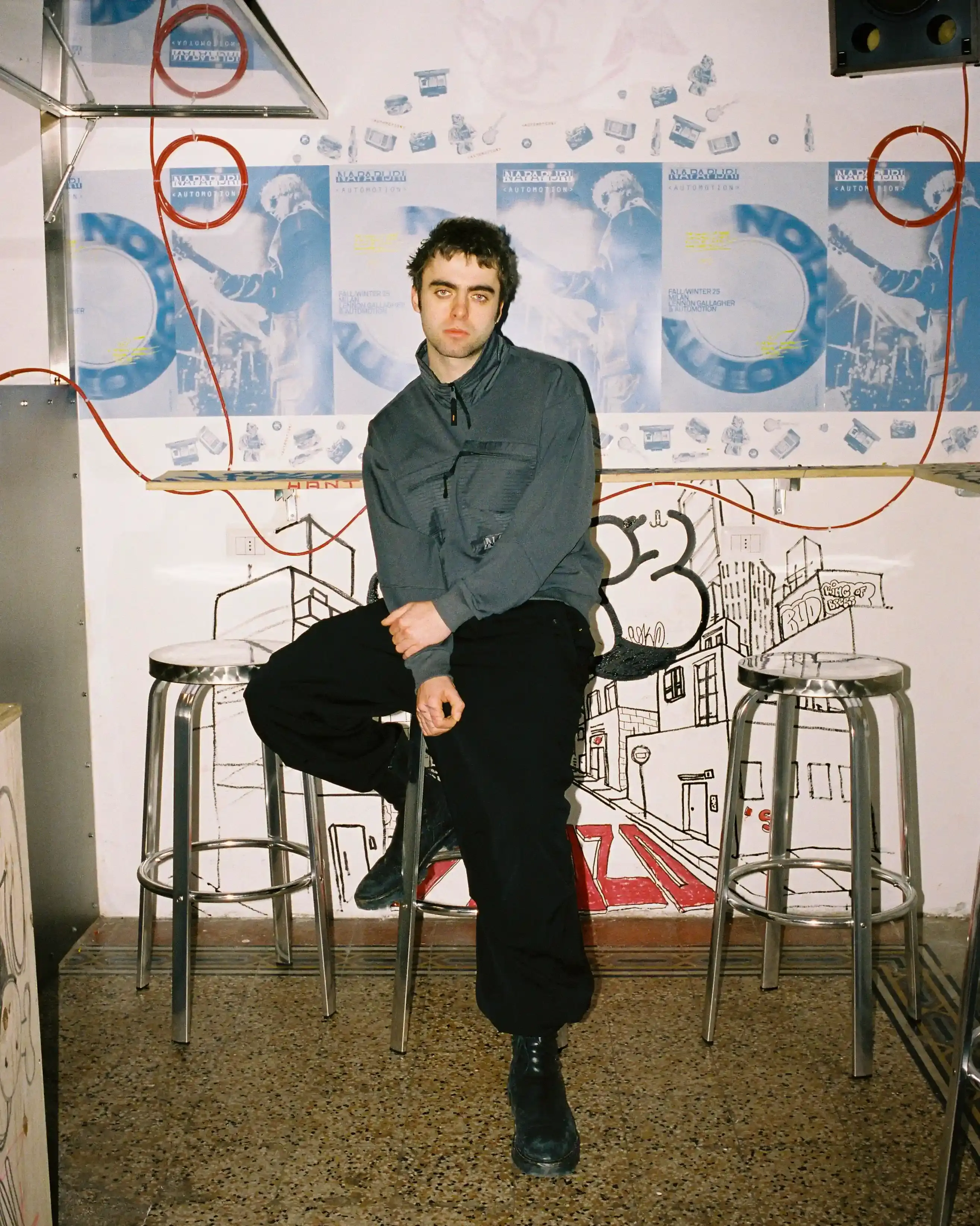 © Casawi | quadronnodistrict image of Lennon Gallagher, featuring a Q&A format discussion about his modeling work with Napapijri, his band activities, daily routines, and personal influences including David Bowie. The article reveals his casual approach to life, balancing music practice with modeling, and his preference for a laid-back lifestyle. shoot by quadronnodistrict (image 13 of 13)