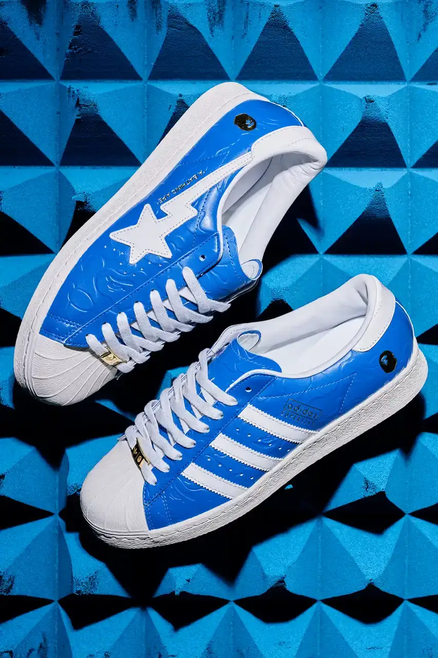 ADIDAS AND BAPE UNITE FOR FRESH COLLECTION AFTER TWO DECADES This article discusses the new collaboration between adidas and A Bathing Ape (BAPE). It details their latest capsule collection centered around the SSTR V BAPE sneaker, which reimagines the classic Superstar silhouette. The article describes the sneaker's design features, available colorways for adults and children, and mentions the accompanying apparel and accessories including tracksuits, hoodies, t-shirts, caps, pouches, and socks. It concludes with information about the April 5th release date through the CONFIRMED app and select retailers. (image 2 of 11)