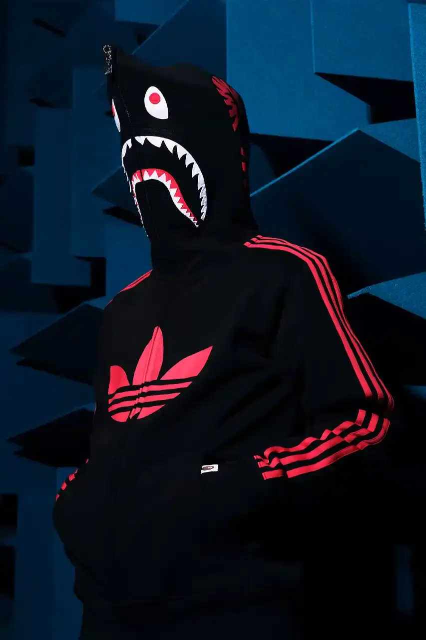 ADIDAS AND BAPE UNITE FOR FRESH COLLECTION AFTER TWO DECADES This article discusses the new collaboration between adidas and A Bathing Ape (BAPE). It details their latest capsule collection centered around the SSTR V BAPE sneaker, which reimagines the classic Superstar silhouette. The article describes the sneaker's design features, available colorways for adults and children, and mentions the accompanying apparel and accessories including tracksuits, hoodies, t-shirts, caps, pouches, and socks. It concludes with information about the April 5th release date through the CONFIRMED app and select retailers.