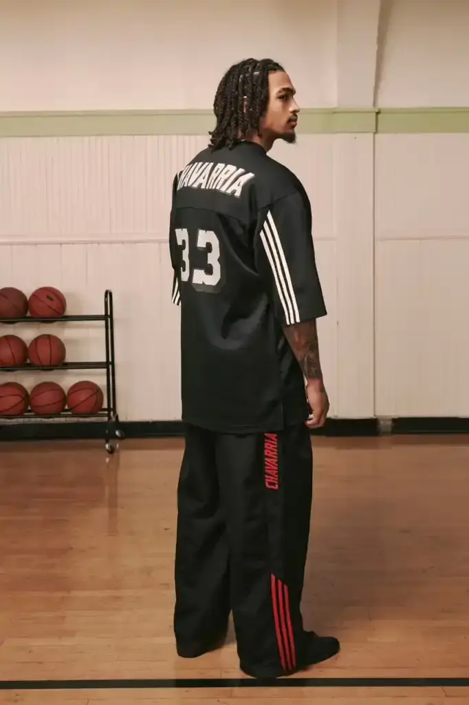 ADIDAS ORIGINALS TEAMS WITH WILLY CHAVARRIA ON CHICANO-INSPIRED COLLECTION image of the Spring/Summer 2025 collaboration between adidas Originals and designer Willy Chavarria. The collection celebrates Chicano culture through fashion, featuring oversized silhouettes and Mexican cultural symbols. Key pieces include tracksuits with Three Stripes, redesigned Trefoil logos with rose embroidery, co-branded hoodies with red and green panels, and the revamped 1978 Jabbar basketball shoe. The collection launches in two drops: May 8 and July 10, available through the CONFIRMED app and select retailers. The campaign was photographed by Carlos Jaramillo in Los Angeles with Chavarria's friends and family. (image 4 of 10)