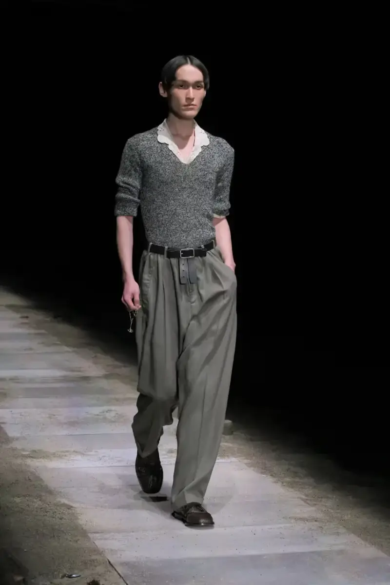 Magliano Models walk on sand-covered runway inside dark gymnasium, wearing layered winter clothing with misaligned buttons and multiple belts from Magliano's FW25 collection. (image 35 of 35)