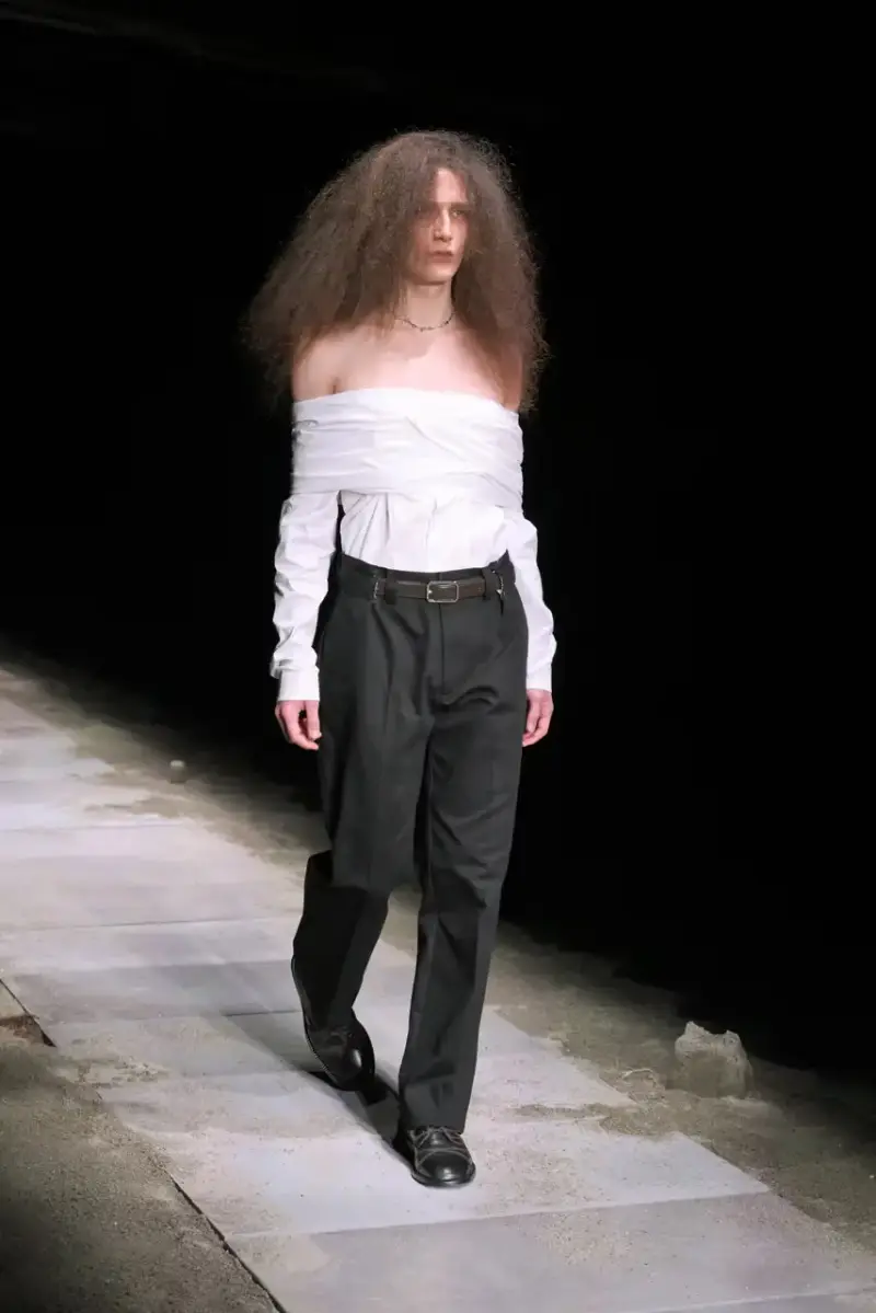Magliano Models walk on sand-covered runway inside dark gymnasium, wearing layered winter clothing with misaligned buttons and multiple belts from Magliano's FW25 collection. (image 3 of 35)