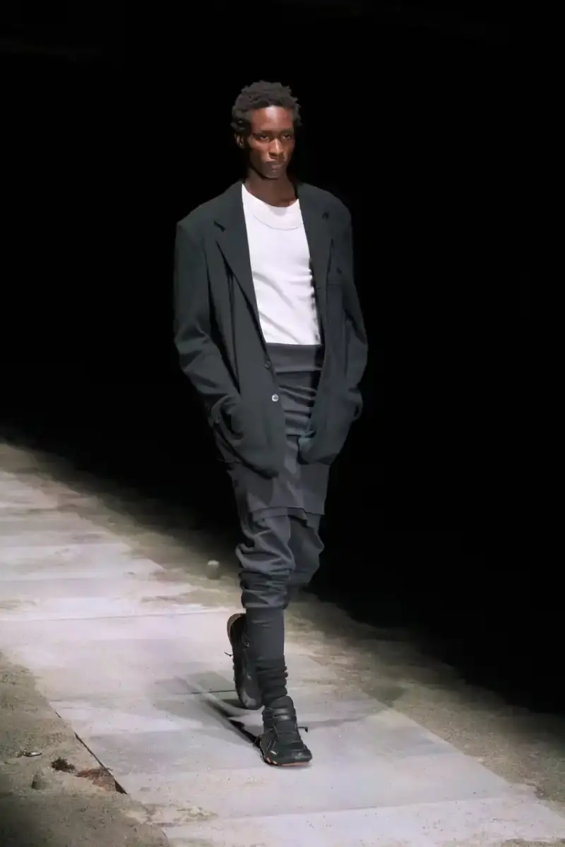 Magliano Models walk on sand-covered runway inside dark gymnasium, wearing layered winter clothing with misaligned buttons and multiple belts from Magliano's FW25 collection. (image 4 of 35)
