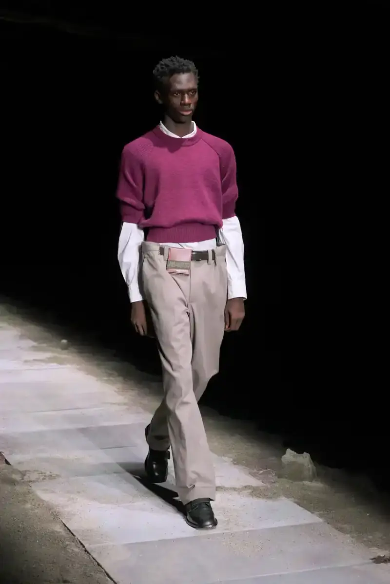 Magliano Models walk on sand-covered runway inside dark gymnasium, wearing layered winter clothing with misaligned buttons and multiple belts from Magliano's FW25 collection. (image 14 of 35)