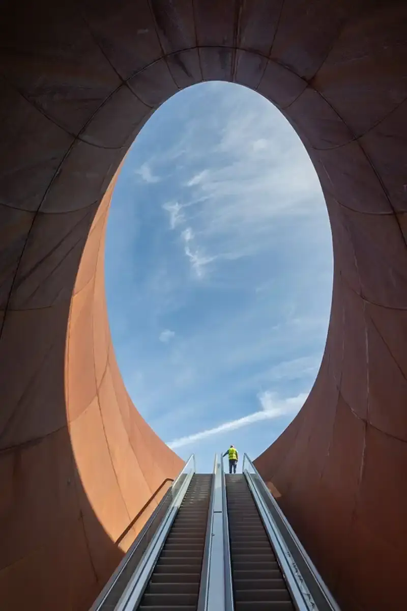 ANISH KAPOOR'S NAPLES SUBWAY STATION OPENS TODAY Two contrasting subway station entrances in Naples designed by Anish Kapoor: one features curved weathering steel panels with organic texture rising from plaza pavement, the other shows a sunken aluminum tube entrance with brushed metal finish reflecting surrounding buildings (image 7 of 7)