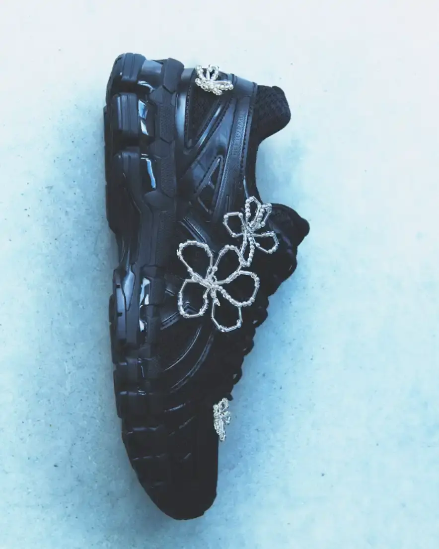 ASICS AND COMPLETEDWORKS RELEASE GEL-KAYANO 20 COLLABORATION A photograph shows a pair of ASICS GEL-KAYANO 20 sneakers modified with sculptural jewelry elements like pearls and floral motifs. (image 3 of 6)