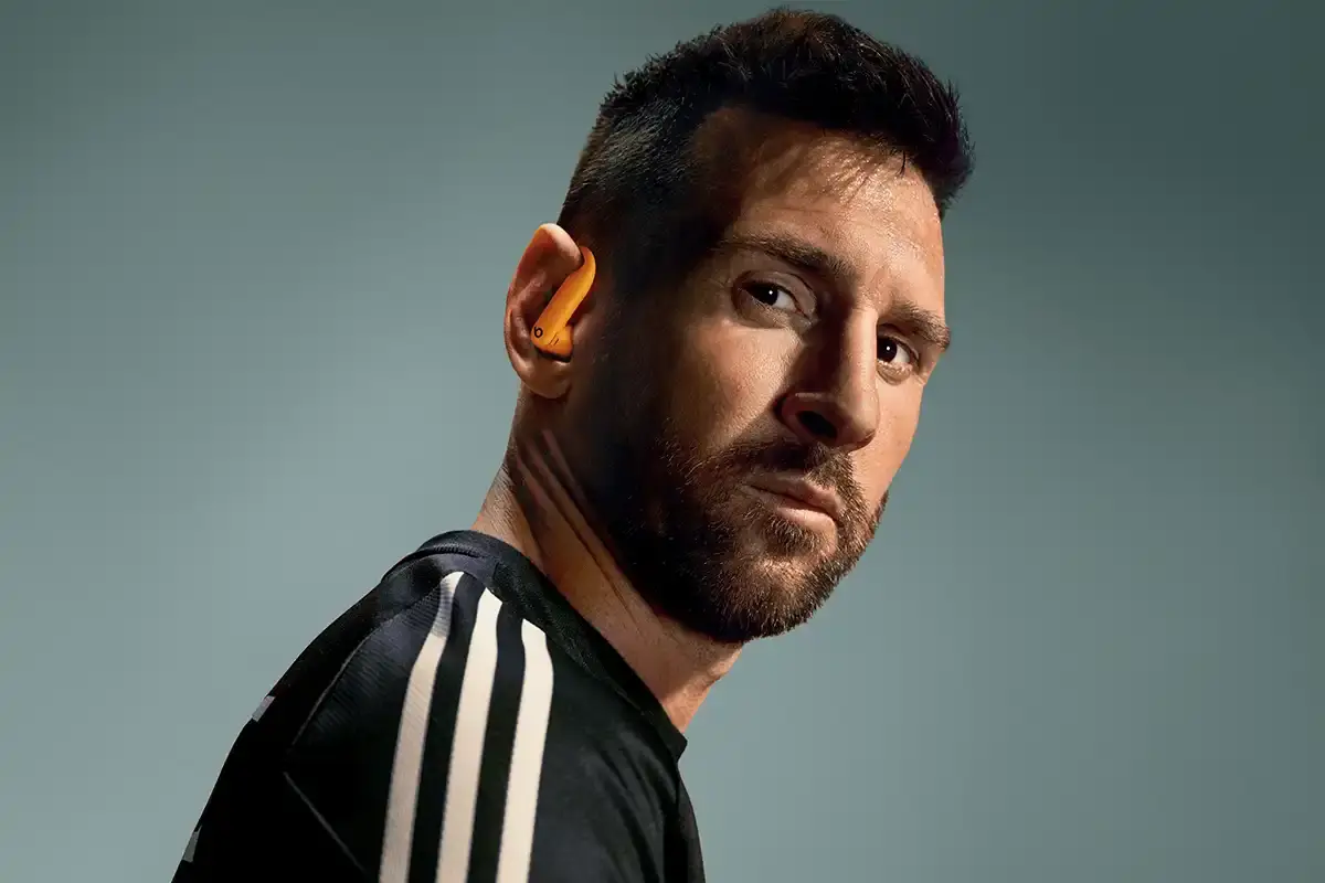 Beats Lionel Messi wear Powerbeats Pro 2 wireless earphones in Electric Orange color, showing ear hooks and charging case with wireless charging capability.