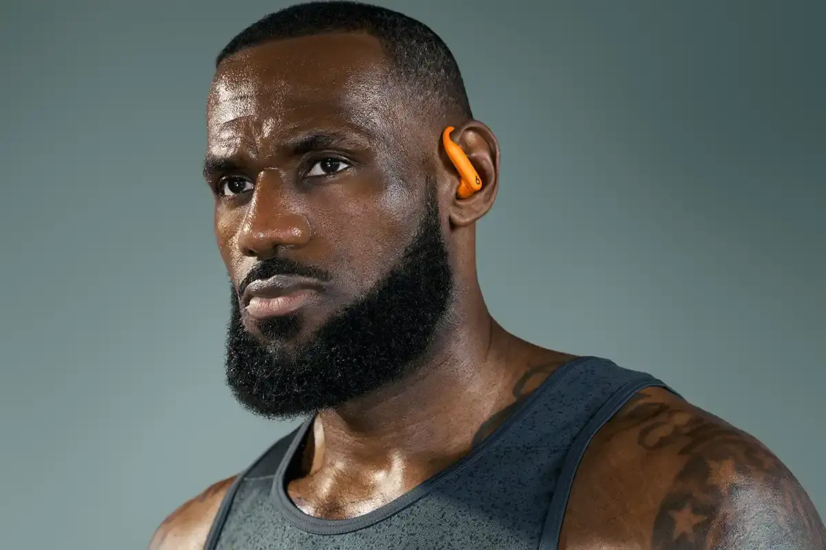 Beats Lebron James wear Powerbeats Pro 2 wireless earphones in Electric Orange color, showing ear hooks and charging case with wireless charging capability.