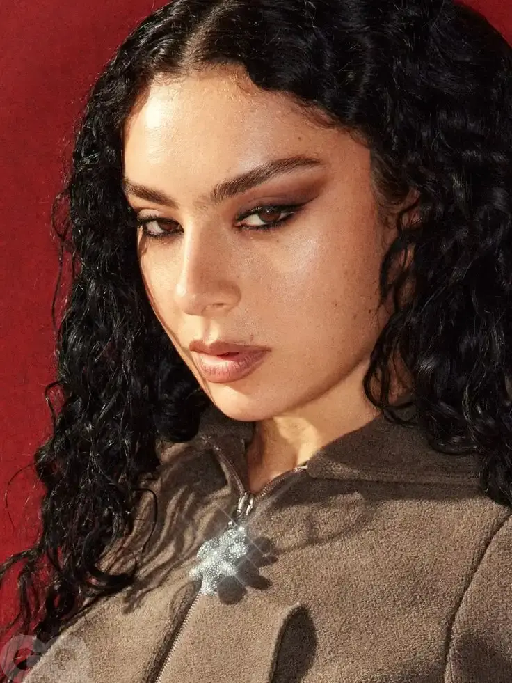 Charli XCX performing on stage, wearing smokey eye makeup and her signature tousled dark curls
