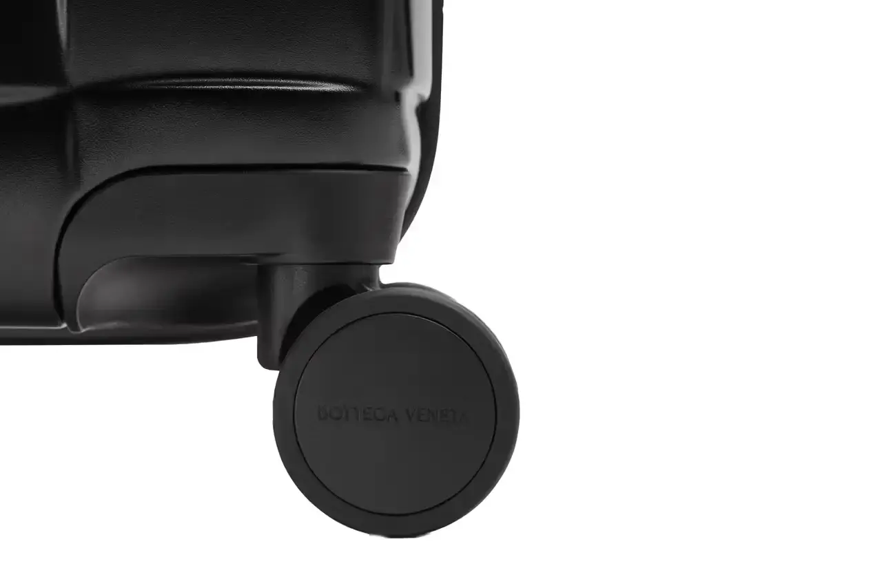 Bottega Veneta Bottega Veneta Odyssey carry-on suitcase with textured polycarbonate shell featuring 3D Intreccio pattern, silver hardware, and brown calfskin leather handles. The wheeled luggage is shown in a three-quarter view displaying its structured design and branded details. (image 5 of 7)