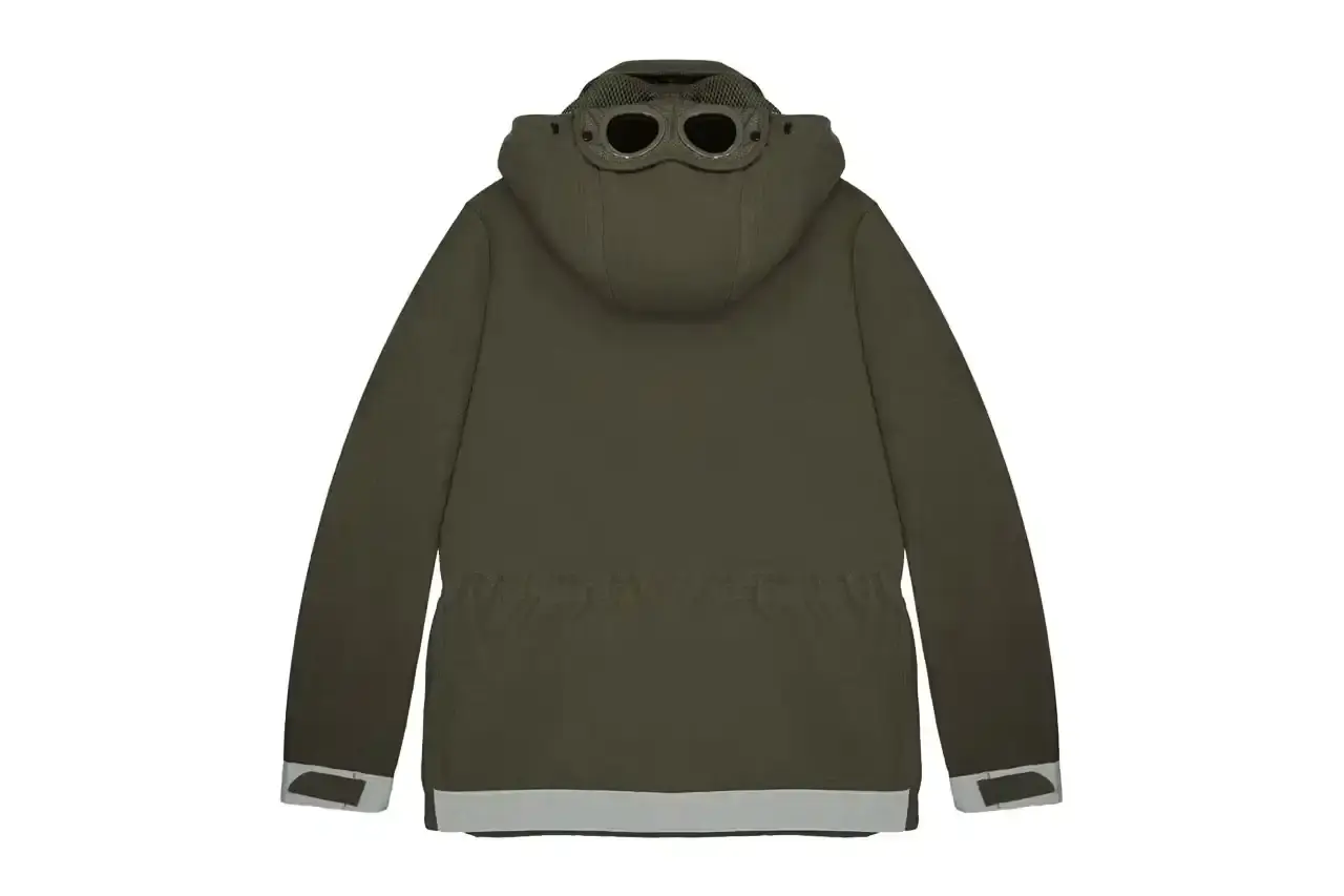 Automobili Amos The C.P. Company x Automobili Amos Mille Jacket shown in signature green color, featuring the distinctive goggle hood design, reflective details, and technical mesh construction. The jacket is photographed against a neutral background, displaying its motorsport-inspired details including the watch viewer window and specialized key pocket. (image 2 of 10)