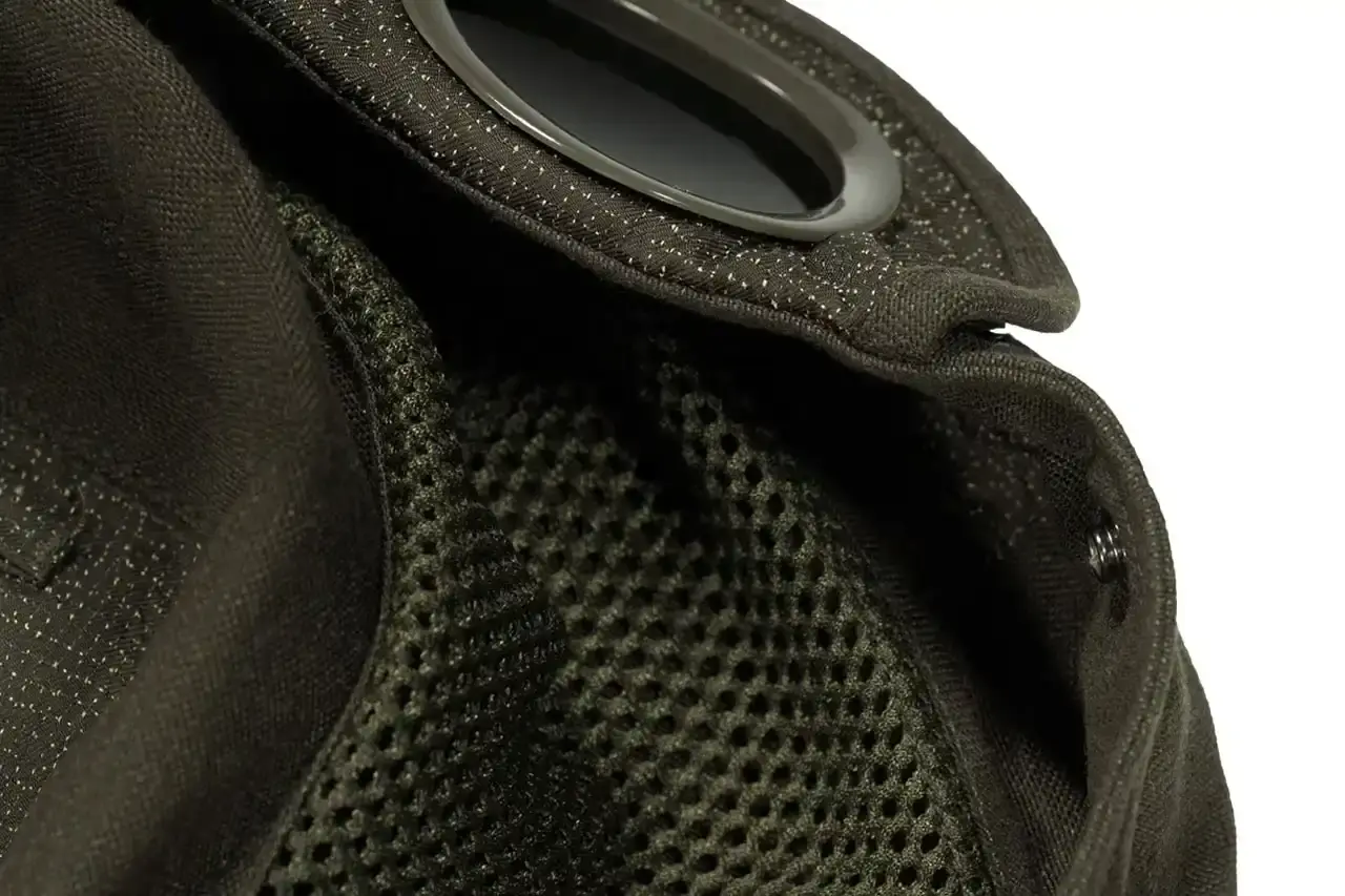 Automobili Amos The C.P. Company x Automobili Amos Mille Jacket shown in signature green color, featuring the distinctive goggle hood design, reflective details, and technical mesh construction. The jacket is photographed against a neutral background, displaying its motorsport-inspired details including the watch viewer window and specialized key pocket. (image 9 of 10)