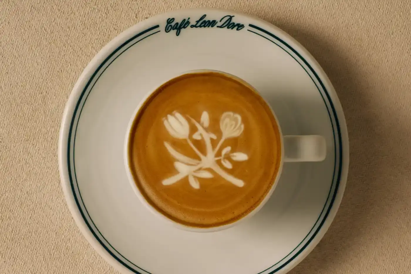 CAFÉ LEON DORE PARTNERS WITH LA MARZOCCO ON EXCLUSIVE COFFEE COLLECTION Image of the collaboration between Café Leon Dore (part of Aimé Leon Dore) and La Marzocco. The partnership features a custom-designed Linea Micra espresso machine in green with brass and walnut details, plus co-branded apparel including aprons, t-shirts, and hats. The collection is available exclusively through Aimé Leon Dore's stores and website. The article provides details about the machine's professional capabilities despite its compact size, and notes that it's being produced in limited quantities. (image 6 of 6)