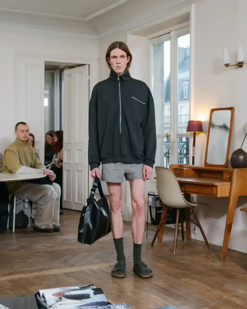 CAMIEL FORTGENS REWORKS DOMESTIC MATERIALS FOR FW26 Camiel Fortgens Fall/Winter 2026 collection shown in Paris apartment, featuring garments made from domestic materials like curtain pleats and sofa leather in earthy tones.