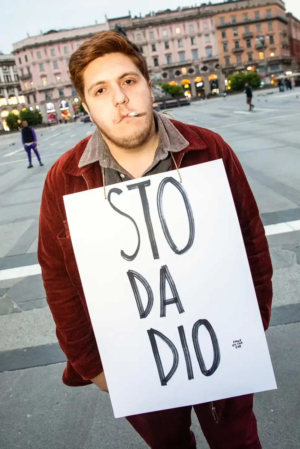 CATTELAN AND BALLARIO TRANSFORM GRIEF INTO DAWN PERFORMANCE IN MILAN'S DUOMO SQUARE Photo of an art performance called "The Cheerful End" organized by artist Maurizio Cattelan and critic Nicolas Ballario in Milan. Held at dawn in Piazza Duomo, participants displayed humorous and philosophical signs about death. The event closed Milan Art Week and was supported by the Museo del Novecento. The performance used irony to encourage public reflection on mortality, with refreshments moved indoors at authorities' request. The article describes how the two creators acted as "accomplices in absurdity" to transform a somber subject into a thought-provoking shared experience. (image 9 of 10)