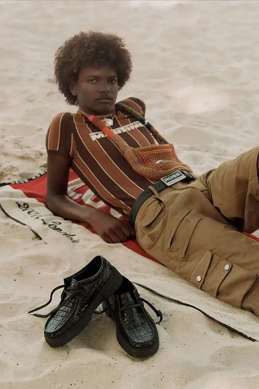 MARTINE ROSE RESHAPES CLARKS HERITAGE IN SS25 COLLECTION An image description for screen readers that highlights the key visual elements of the Clarks x Martine Rose SS25 campaign, focusing on the three shoe styles (Derby, Torview, and Heel) photographed on local beachgoers, showcasing the unique design details, textures, and color palette of the collection. (image 4 of 6)