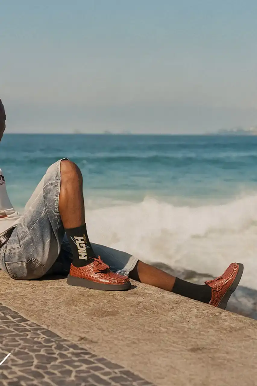 MARTINE ROSE RESHAPES CLARKS HERITAGE IN SS25 COLLECTION An image description for screen readers that highlights the key visual elements of the Clarks x Martine Rose SS25 campaign, focusing on the three shoe styles (Derby, Torview, and Heel) photographed on local beachgoers, showcasing the unique design details, textures, and color palette of the collection. (image 3 of 6)