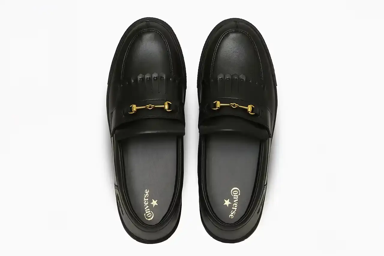 Converse Converse All-Star Coupe GB Loafer shown from side angle, featuring minimalist leather construction, tasseled midfoot strap with embossed star details, and classic Converse sole. Available in black and off-white colorways. (image 2 of 8)