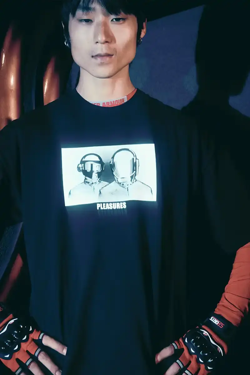 DAFT PUNK TEAMS UP WITH PLEASURES FOR NEW CAPSULE image about fashion collaboration between electronic music duo Daft Punk and streetwear brand PLEASURES. Features clothing and accessories incorporating the musicians' robot helmet imagery, album artwork, and references to their music videos and films. Collection includes hoodies, jackets, jeans, and accessories available July 16, 2025. (image 20 of 28)