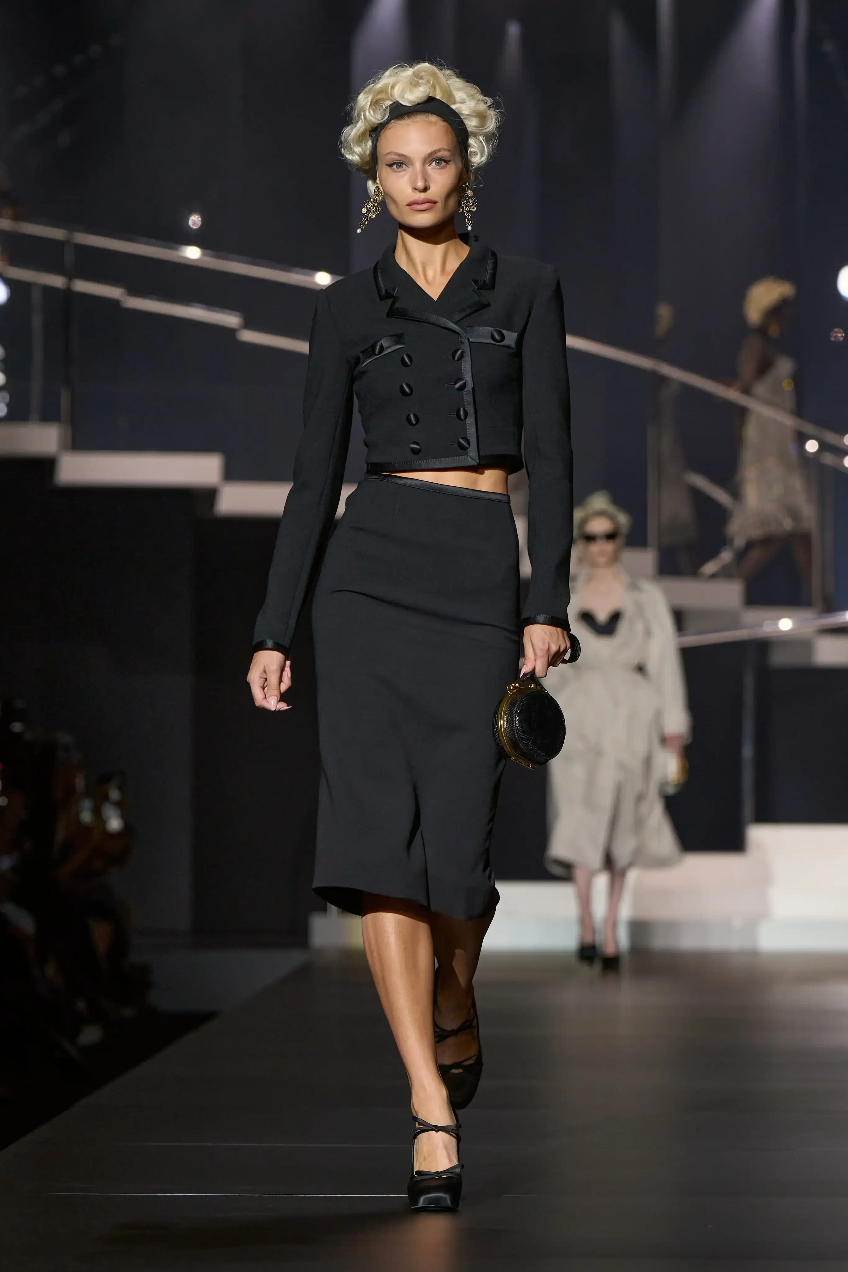 Dolce & Gabbana's Spring/Summer 2025 runway show at Milan Fashion Week showcases a collection inspired by Madonna's iconic style. The presentation features body-contouring designs, including anatomically cut jackets and corsetry details, in materials such as duchesse satin, crepe, tulle, chiffon, lace, and faux fur. The color palette focuses on black, nude, red, and white, with notable pieces including conical bras and oversized cross earrings - signatures of Madonna's most memorable looks. Attended by celebrities like Naomi Campbell and Ashley Graham, the show celebrates Madonna's enduring influence on fashion and her ability to challenge societal norms while remaining true to herself. This collection reinforces Dolce & Gabbana's commitment to empowering women's fashion and highlights the lasting impact of cultural icons on design (image 3 of 9)