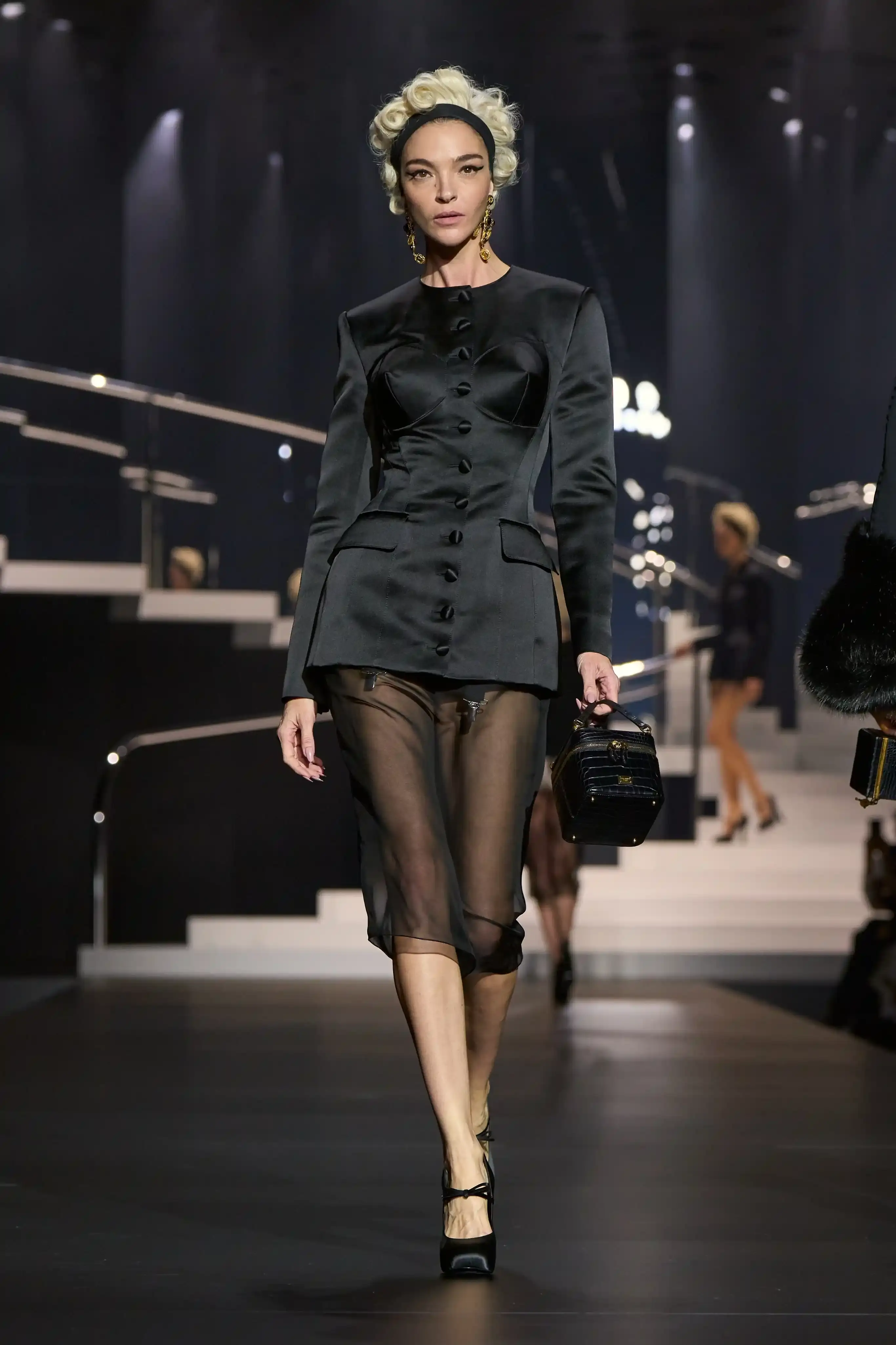 Dolce & Gabbana's Spring/Summer 2025 runway show at Milan Fashion Week showcases a collection inspired by Madonna's iconic style. The presentation features body-contouring designs, including anatomically cut jackets and corsetry details, in materials such as duchesse satin, crepe, tulle, chiffon, lace, and faux fur. The color palette focuses on black, nude, red, and white, with notable pieces including conical bras and oversized cross earrings - signatures of Madonna's most memorable looks. Attended by celebrities like Naomi Campbell and Ashley Graham, the show celebrates Madonna's enduring influence on fashion and her ability to challenge societal norms while remaining true to herself. This collection reinforces Dolce & Gabbana's commitment to empowering women's fashion and highlights the lasting impact of cultural icons on design (image 9 of 9)