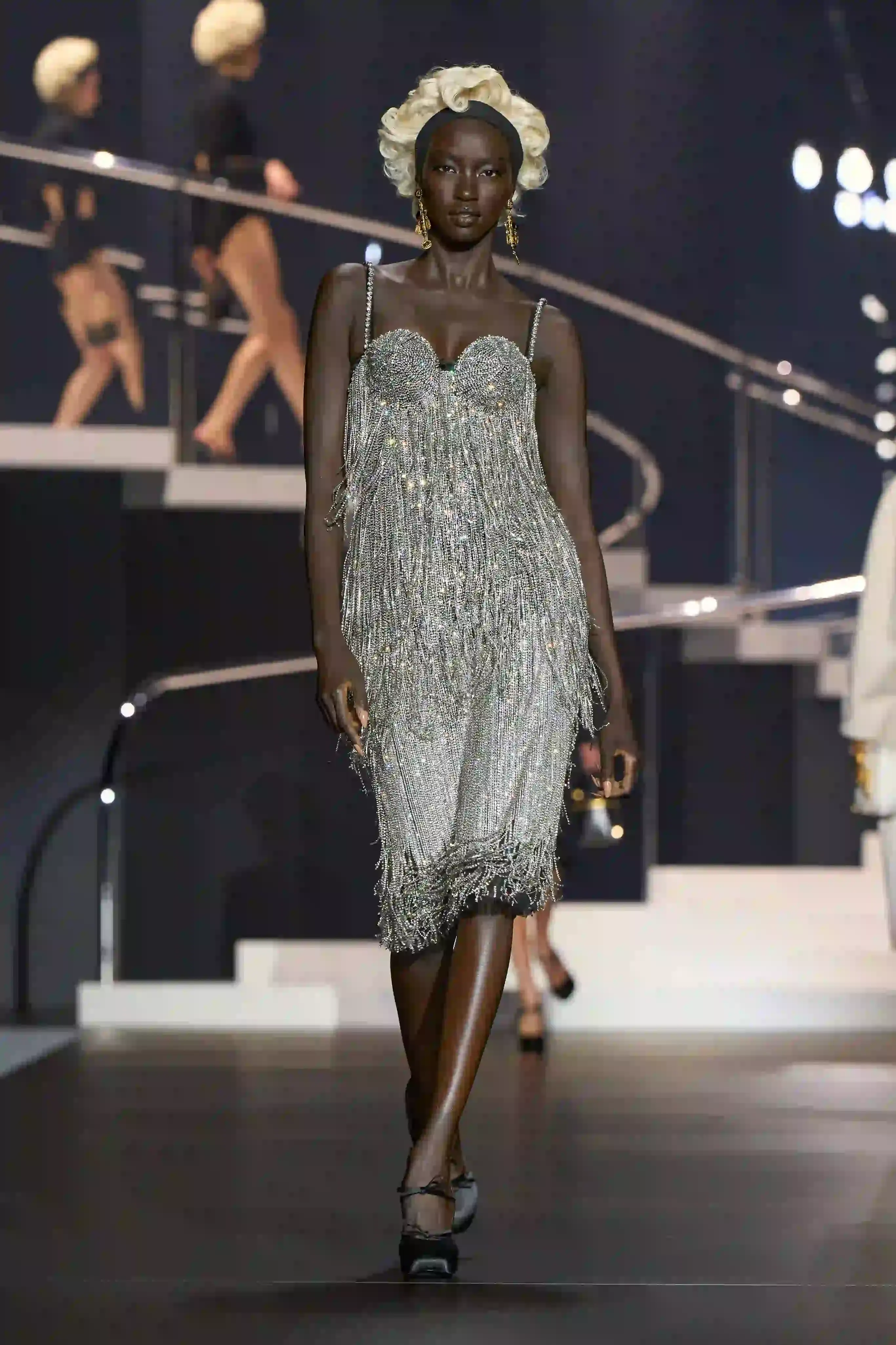 Dolce & Gabbana's Spring/Summer 2025 runway show at Milan Fashion Week showcases a collection inspired by Madonna's iconic style. The presentation features body-contouring designs, including anatomically cut jackets and corsetry details, in materials such as duchesse satin, crepe, tulle, chiffon, lace, and faux fur. The color palette focuses on black, nude, red, and white, with notable pieces including conical bras and oversized cross earrings - signatures of Madonna's most memorable looks. Attended by celebrities like Naomi Campbell and Ashley Graham, the show celebrates Madonna's enduring influence on fashion and her ability to challenge societal norms while remaining true to herself. This collection reinforces Dolce & Gabbana's commitment to empowering women's fashion and highlights the lasting impact of cultural icons on design (image 4 of 9)