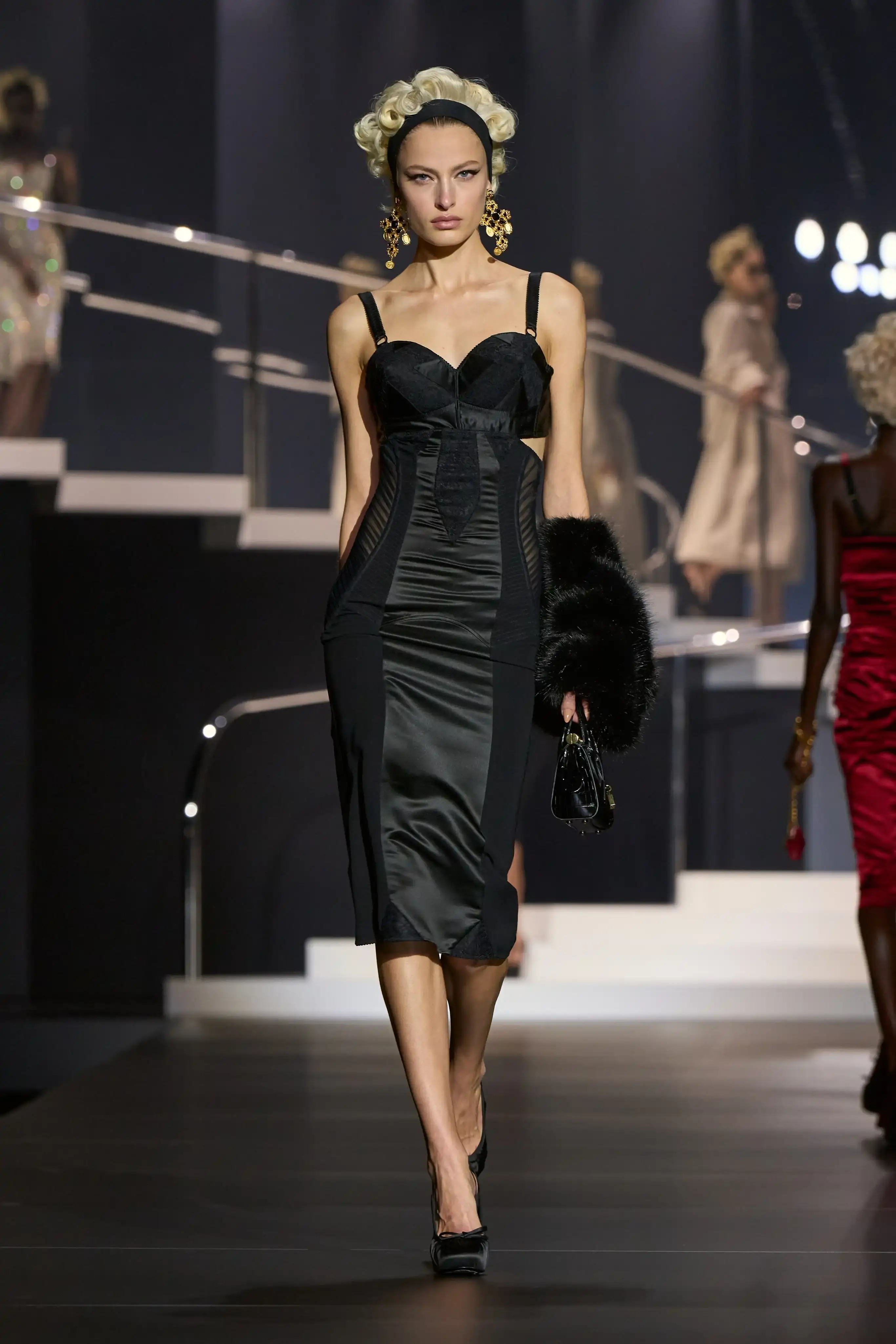Dolce & Gabbana's Spring/Summer 2025 runway show at Milan Fashion Week showcases a collection inspired by Madonna's iconic style. The presentation features body-contouring designs, including anatomically cut jackets and corsetry details, in materials such as duchesse satin, crepe, tulle, chiffon, lace, and faux fur. The color palette focuses on black, nude, red, and white, with notable pieces including conical bras and oversized cross earrings - signatures of Madonna's most memorable looks. Attended by celebrities like Naomi Campbell and Ashley Graham, the show celebrates Madonna's enduring influence on fashion and her ability to challenge societal norms while remaining true to herself. This collection reinforces Dolce & Gabbana's commitment to empowering women's fashion and highlights the lasting impact of cultural icons on design (image 2 of 9)