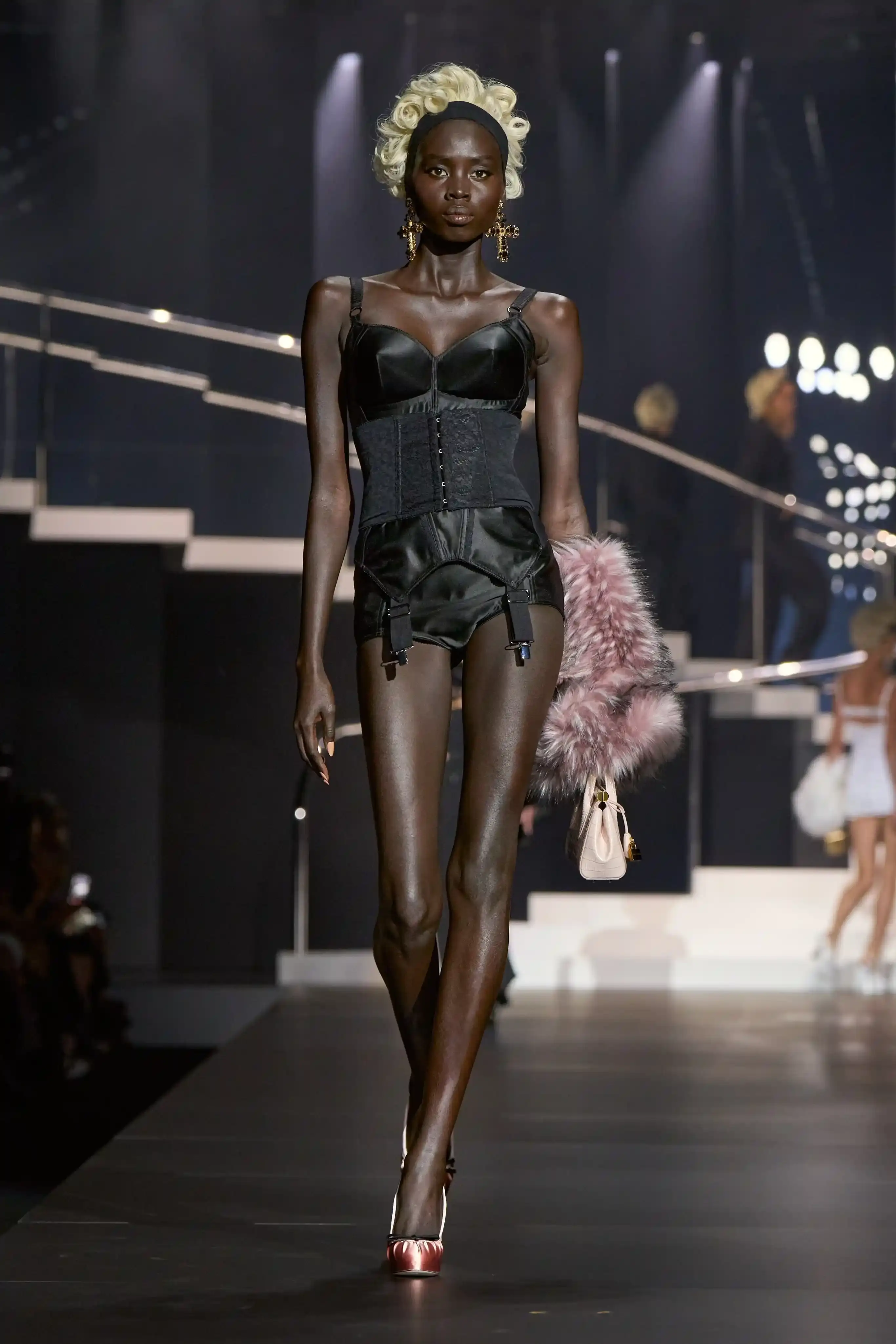 Dolce & Gabbana's Spring/Summer 2025 runway show at Milan Fashion Week showcases a collection inspired by Madonna's iconic style. The presentation features body-contouring designs, including anatomically cut jackets and corsetry details, in materials such as duchesse satin, crepe, tulle, chiffon, lace, and faux fur. The color palette focuses on black, nude, red, and white, with notable pieces including conical bras and oversized cross earrings - signatures of Madonna's most memorable looks. Attended by celebrities like Naomi Campbell and Ashley Graham, the show celebrates Madonna's enduring influence on fashion and her ability to challenge societal norms while remaining true to herself. This collection reinforces Dolce & Gabbana's commitment to empowering women's fashion and highlights the lasting impact of cultural icons on design (image 7 of 9)