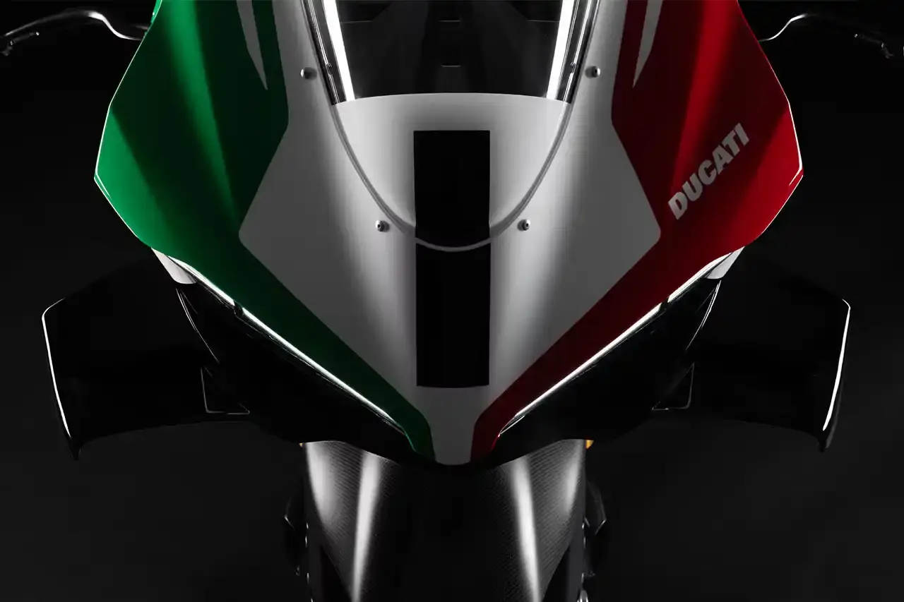Ducati A side profile view of the Ducati Panigale V4 Tricolore motorcycle, showcasing its sleek racing design with asymmetrical Italian flag-inspired color scheme. The bike features carbon fiber rims, a racing-inspired silhouette, and a distinctive checkered flag motif, highlighting its special edition status and high-performance engineering.
