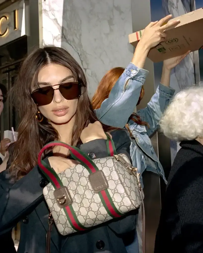 EMILY RATAJKOWSKI STARS IN NEW GUCCI CAMPAIGN image of Emily Ratajkowski modeling Gucci handbags with the signature GG monogram pattern. Photographed in Cannes by Daniel Arnold, the campaign highlights heritage-inspired bag designs including the new Giglio model and updated Ophidia series. Images show the model in various city and coastal locations demonstrating how the monogram pattern adapts to different settings and occasions. (image 2 of 4)