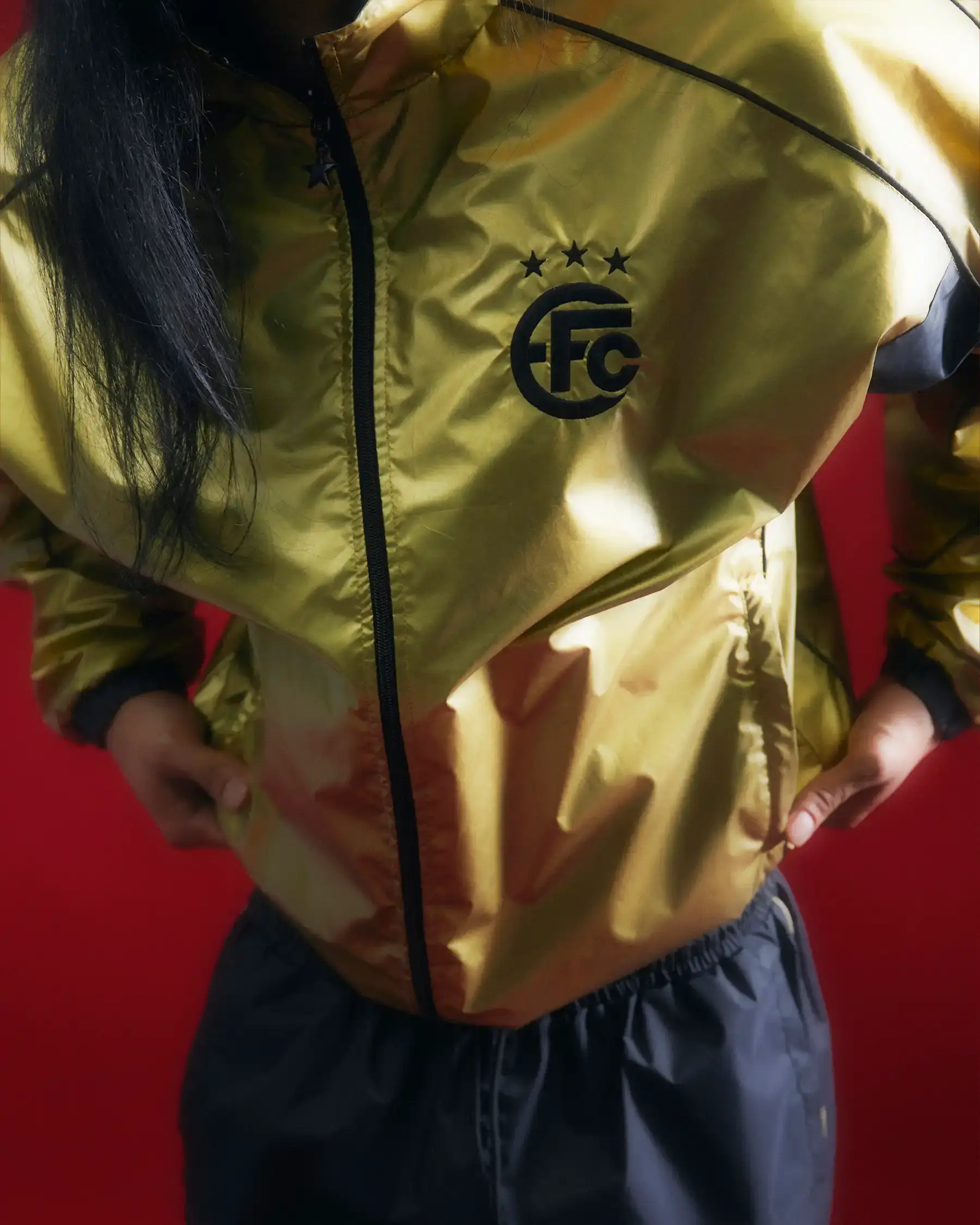 Equipo FC Image shows Equipo FC's reversible "Winners Tracksuit" displayed from both sides - one completely gold and one black with gold details. The tracksuit features star patterns and an embroidered crest, inspired by iconic 2000s football team apparel. (image 2 of 7)