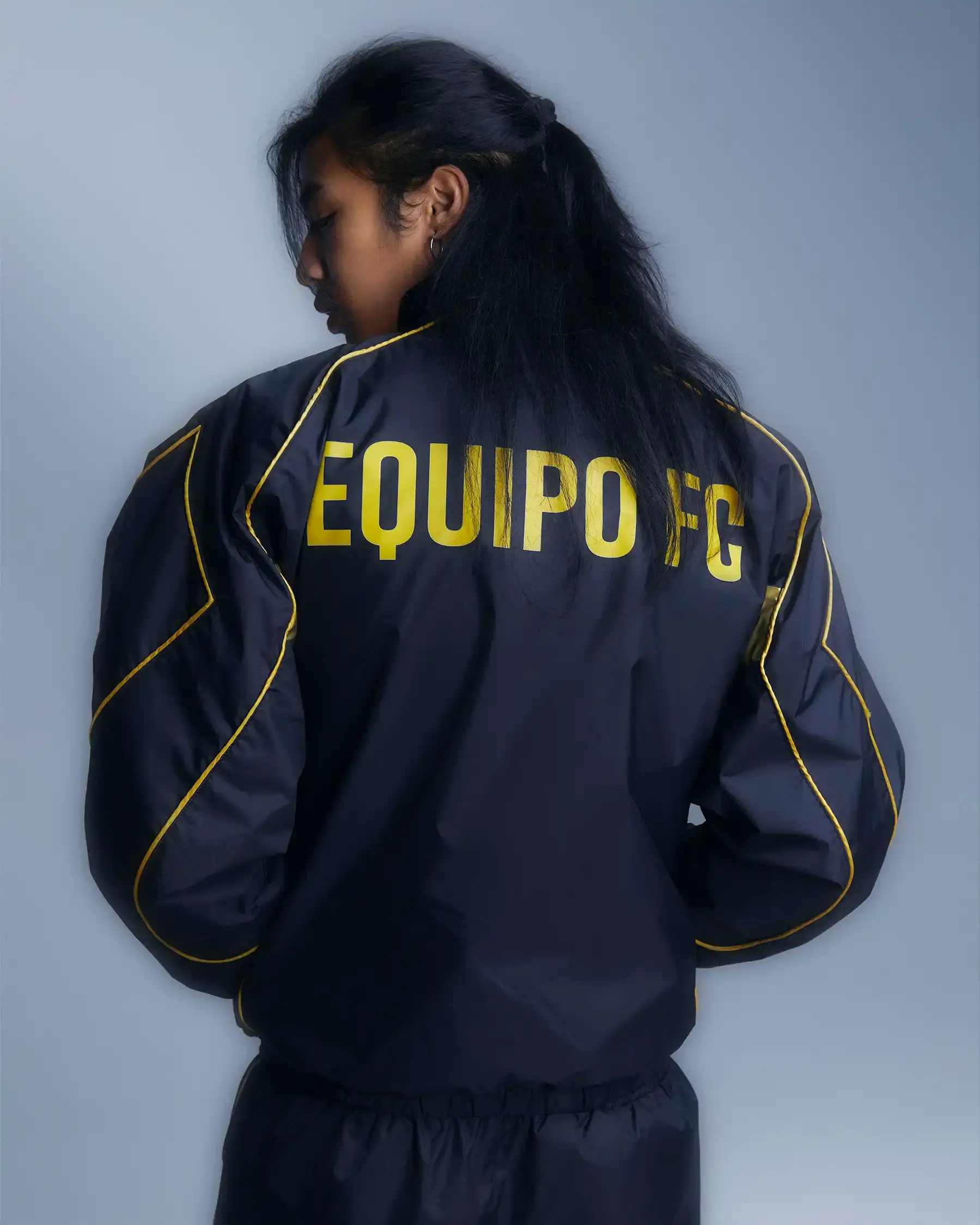 Equipo FC Image shows Equipo FC's reversible "Winners Tracksuit" displayed from both sides - one completely gold and one black with gold details. The tracksuit features star patterns and an embroidered crest, inspired by iconic 2000s football team apparel. (image 7 of 7)