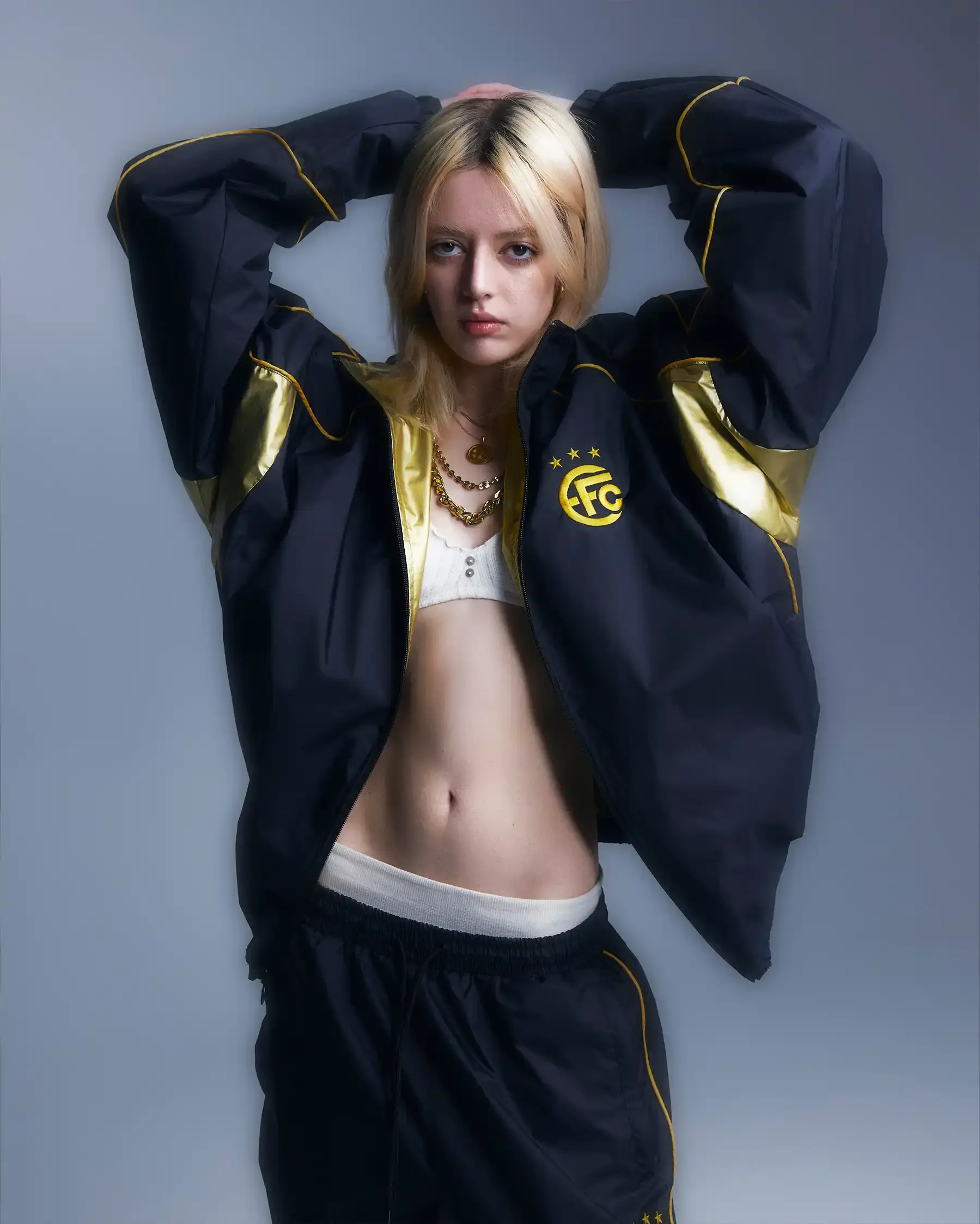 Equipo FC Image shows Equipo FC's reversible "Winners Tracksuit" displayed from both sides - one completely gold and one black with gold details. The tracksuit features star patterns and an embroidered crest, inspired by iconic 2000s football team apparel. (image 5 of 7)