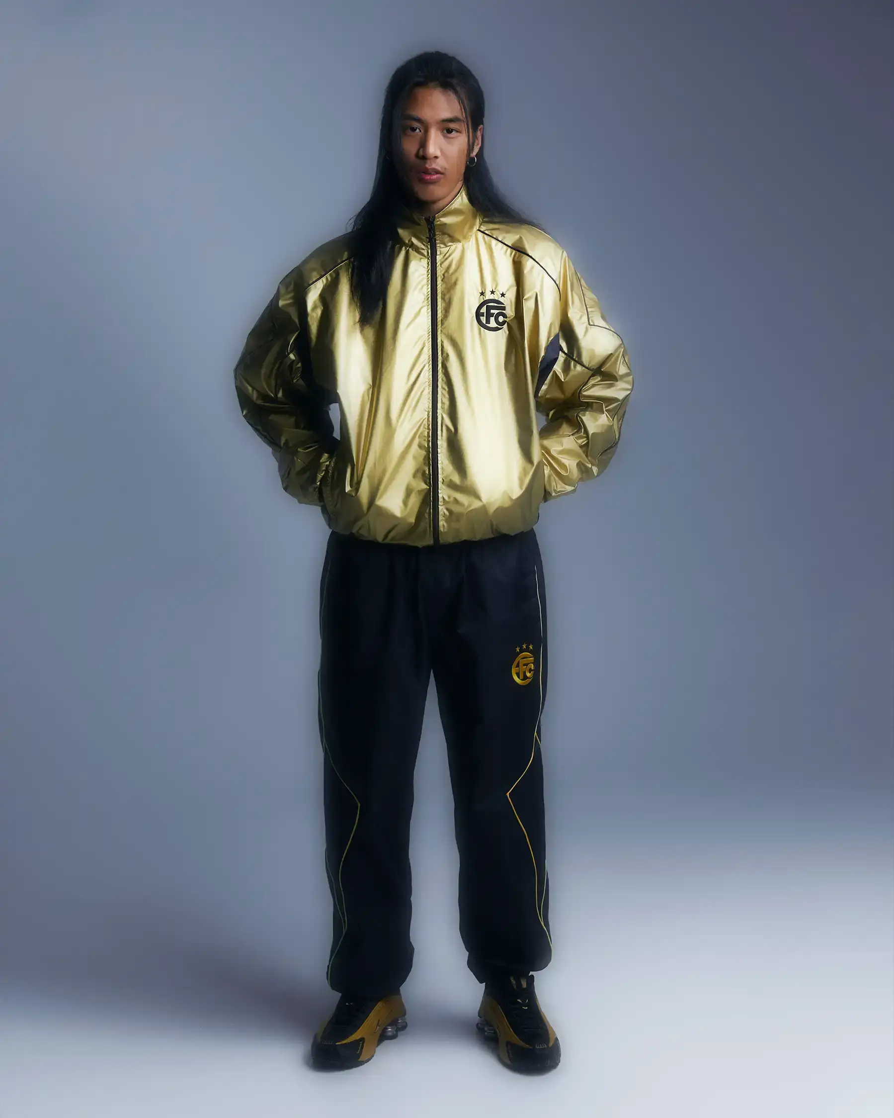 Equipo FC Image shows Equipo FC's reversible "Winners Tracksuit" displayed from both sides - one completely gold and one black with gold details. The tracksuit features star patterns and an embroidered crest, inspired by iconic 2000s football team apparel.