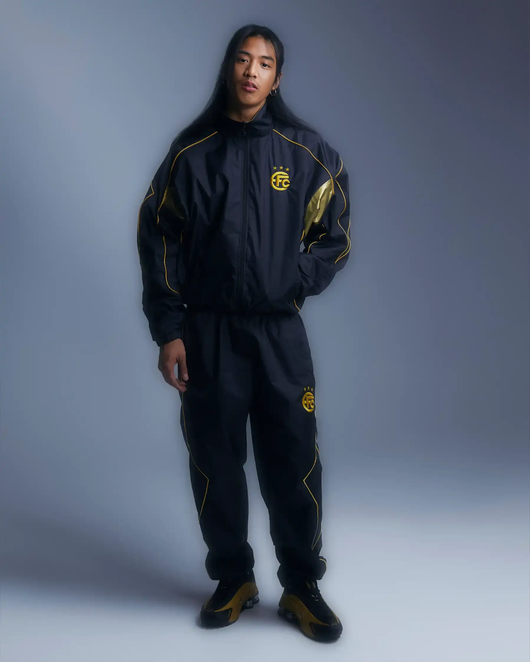Equipo FC Image shows Equipo FC's reversible "Winners Tracksuit" displayed from both sides - one completely gold and one black with gold details. The tracksuit features star patterns and an embroidered crest, inspired by iconic 2000s football team apparel. (image 6 of 7)