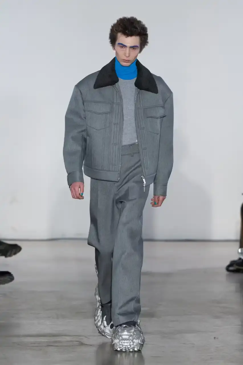 Feng Chen Wang Runway image of a model wearing Feng Chen Wang's Fall/Winter 2025 collection, showcasing oversized ceramic-textured UGG slippers and layered outerwear inspired by mythical Chinese creatures from the Shan Hai Jing text (image 5 of 11)