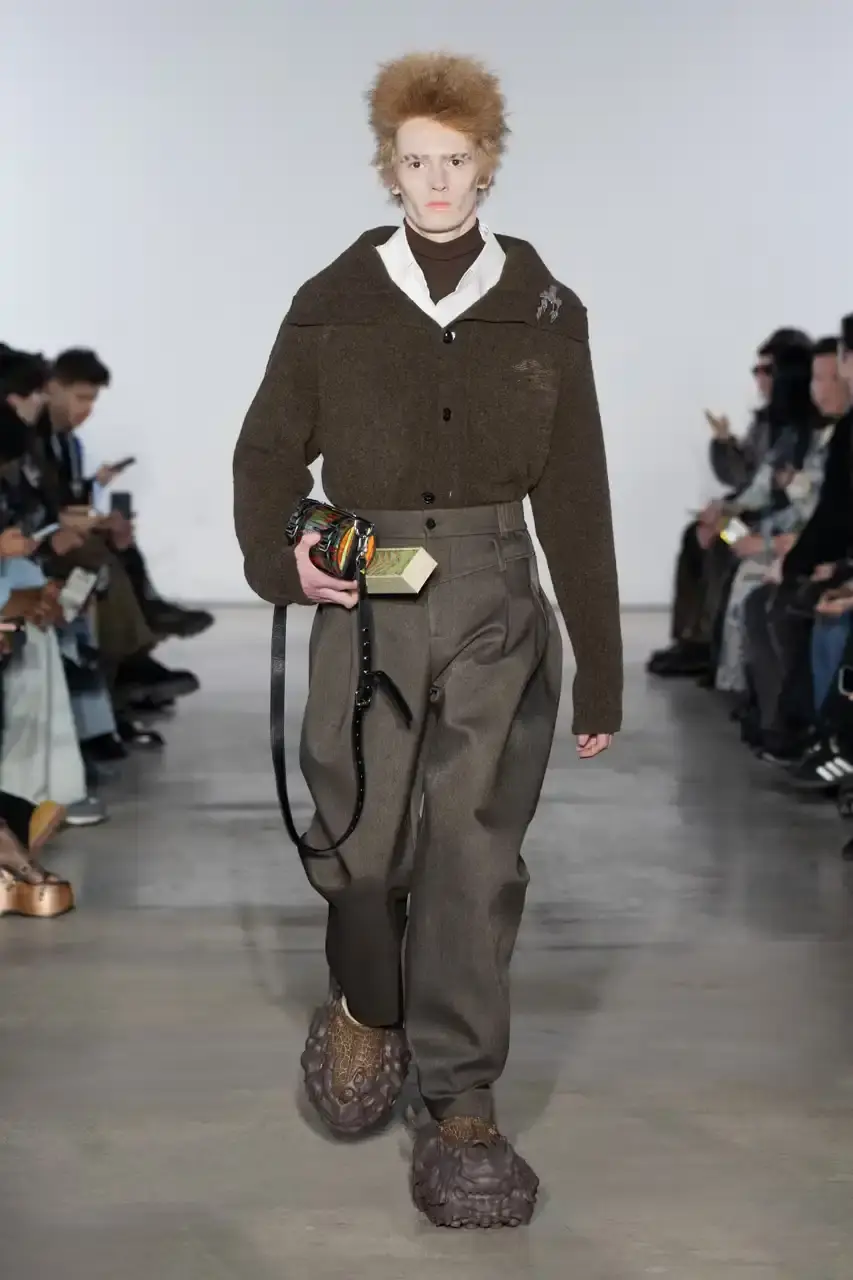 Feng Chen Wang Runway image of a model wearing Feng Chen Wang's Fall/Winter 2025 collection, showcasing oversized ceramic-textured UGG slippers and layered outerwear inspired by mythical Chinese creatures from the Shan Hai Jing text