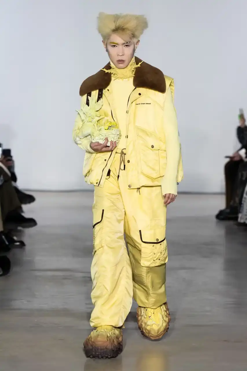 Feng Chen Wang Runway image of a model wearing Feng Chen Wang's Fall/Winter 2025 collection, showcasing oversized ceramic-textured UGG slippers and layered outerwear inspired by mythical Chinese creatures from the Shan Hai Jing text (image 9 of 11)