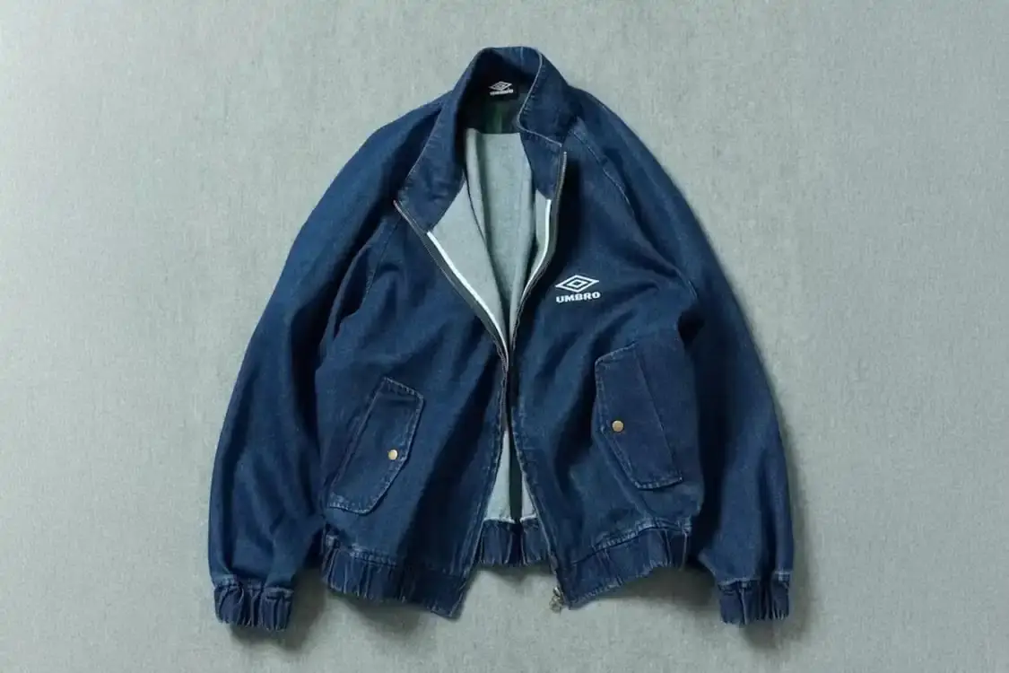FREAK'S STORE X UMBRO DENIM BLOUSON DROPS LATE JANUARY Japanese retailer FREAK'S STORE partners with British sportswear brand UMBRO on a denim blouson jacket featuring a stand collar, minimal branding, and Black Watch tartan interior details, releasing late January 2026.