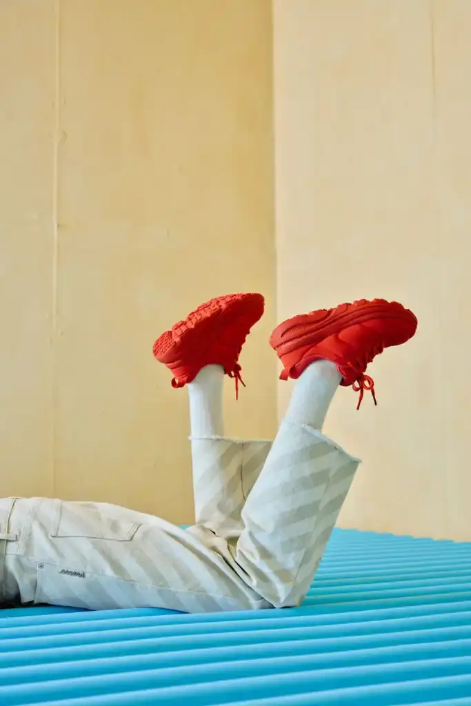 HOKA AND MARNI UNVEIL NEW SNEAKER PARTNERSHIP IN MILAN photo of the collaboration between athletic footwear brand Hoka and fashion label Marni on their new Bondi B3LS sneaker. It details the shoe's technical features including a cushioned sole, mesh upper with TPU reinforcements, and rubber outsole with traction lugs. The piece describes the sneaker's four color options (red, beige, blue, brown) and three interchangeable lace styles. The article also reports on the Milan launch event at Villa Clea featuring foam installations by Finemateria, performances by artist Marta Del Grandi and dancers Federica D'Aversa and Rafael Candela, plus a multisensory dining experience by Mimosa Milano. The sneakers are available for €395 on both brands' websites.