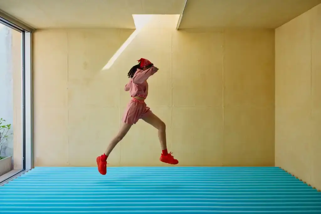 Photo of the collaboration between athletic footwear brand Hoka and fashion label Marni on their new Bondi B3LS sneaker. It details the shoe's technical features including a cushioned sole, mesh upper with TPU reinforcements, and rubber outsole with traction lugs. The piece describes the sneaker's four color options (red, beige, blue, brown) and three interchangeable lace styles. The article also reports on the Milan launch event at Villa Clea featuring foam installations by Finemateria, performances by artist Marta Del Grandi and dancers Federica D'Aversa and Rafael Candela, plus a multisensory dining experience by Mimosa Milano. The sneakers are available for €395 on both brands' websites.
