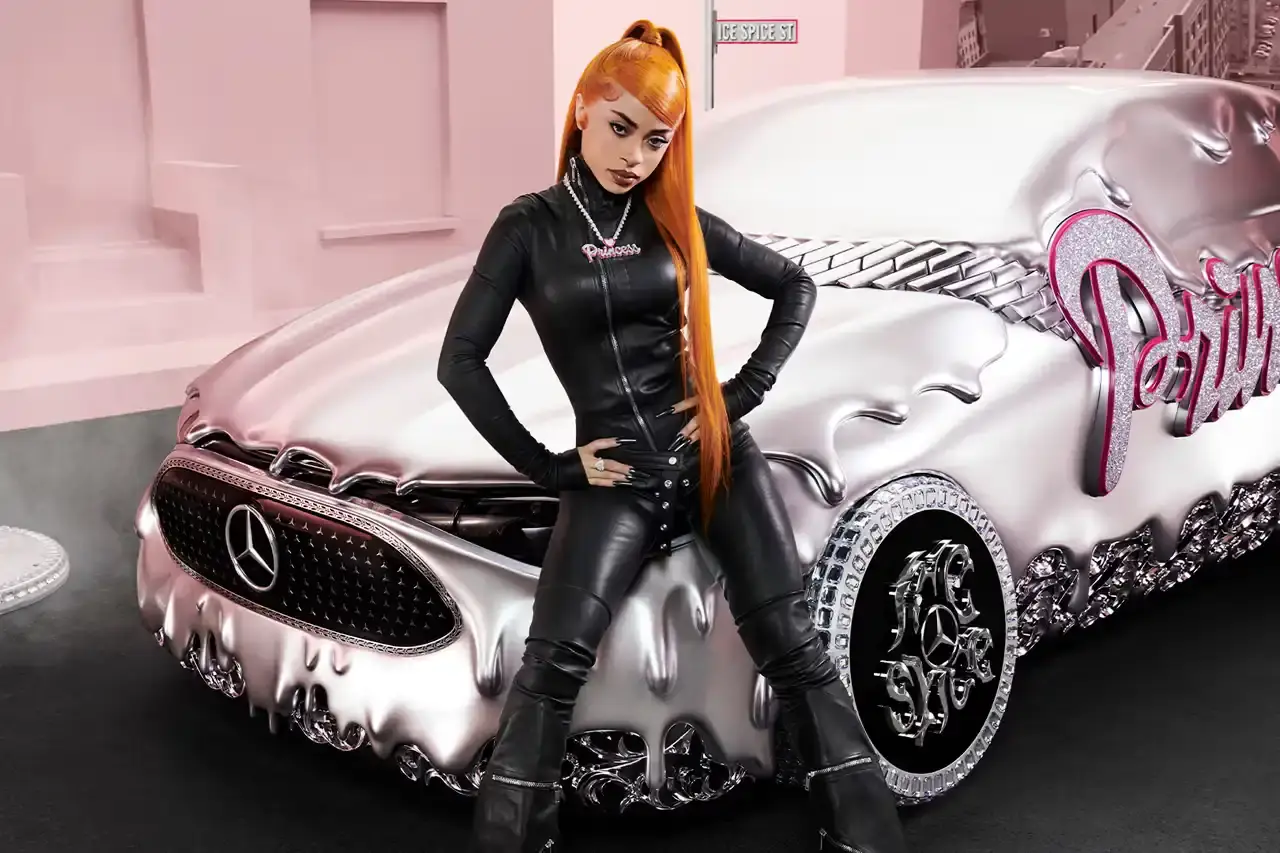 CLA GETS ROYAL CHROME TREATMENT IN ICE SPICE'S MERCEDES COLLAB image of rapper Ice Spice's custom collaboration with Mercedes-Benz, featuring a chrome-finished CLA model with princess-themed detailing. It explains that this is part of Mercedes' "Class of Creators" initiative, where five artists will create custom interpretations of the CLA. The piece details the unveiling event at Mercedes' New York dealership, which included performances from Broadway's "Hell's Kitchen" cast and music by DJ LPX. The article also mentions Ice Spice's upcoming merchandise collection and notes that other collaborators will include Gustaf Westman, KidSuper, League of Legends, and Hot Wheels. (image 2 of 11)