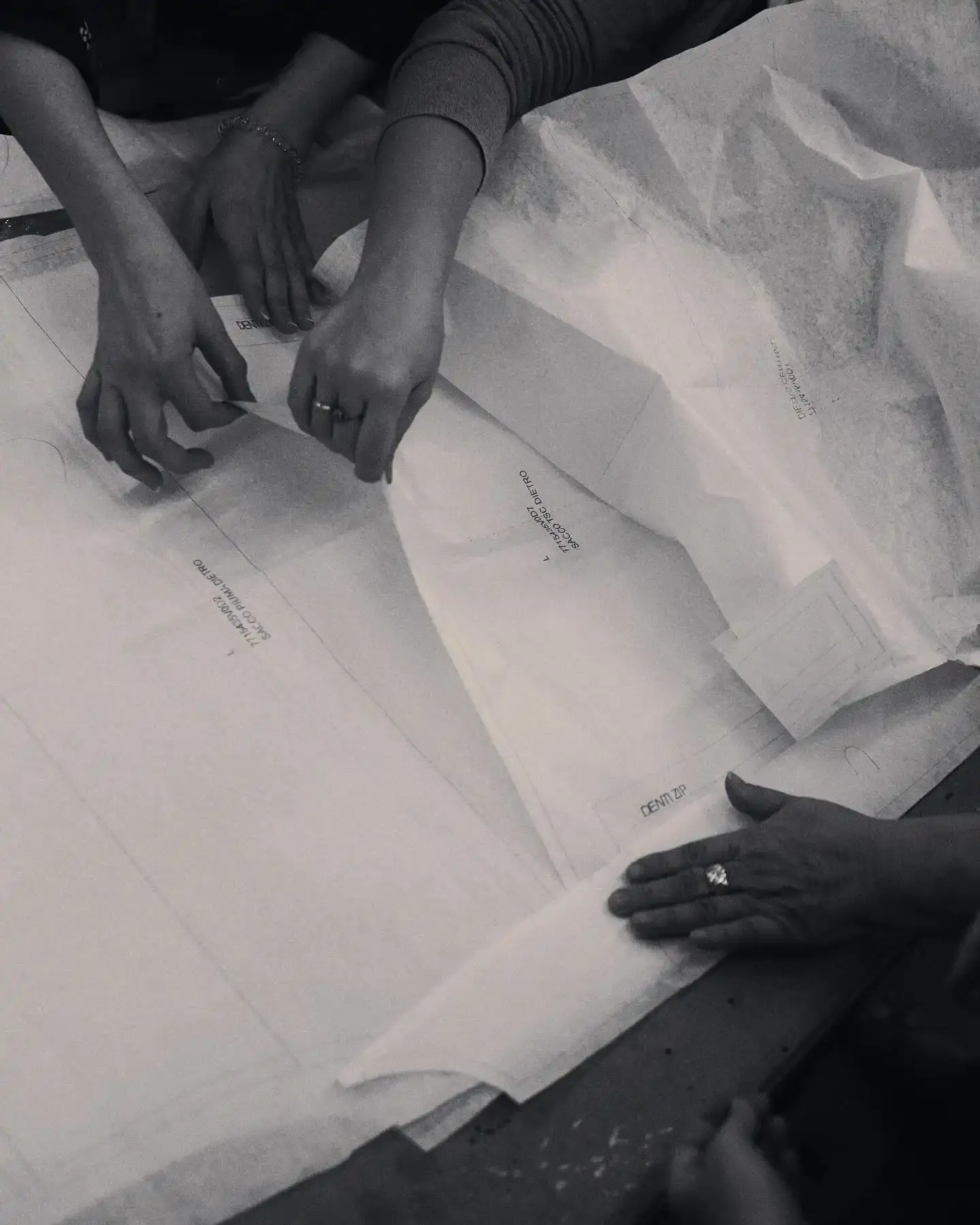 A documentary film scene showing Stone Island's headquarters in Ravarino, with employees working in a well-lit industrial space. The frame captures designers examining fabric swatches, color samples, and innovative garment prototypes, representing the brand's commitment to creative exploration and textile innovation.