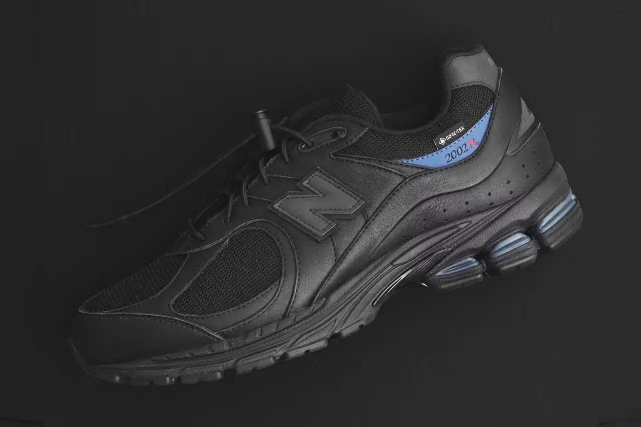 JJJJound JJJJound x New Balance 2002R GORE-TEX sneaker in all-black colorway, featuring mesh and leather construction with a subtle blue heel accent and GORE-TEX waterproof technology