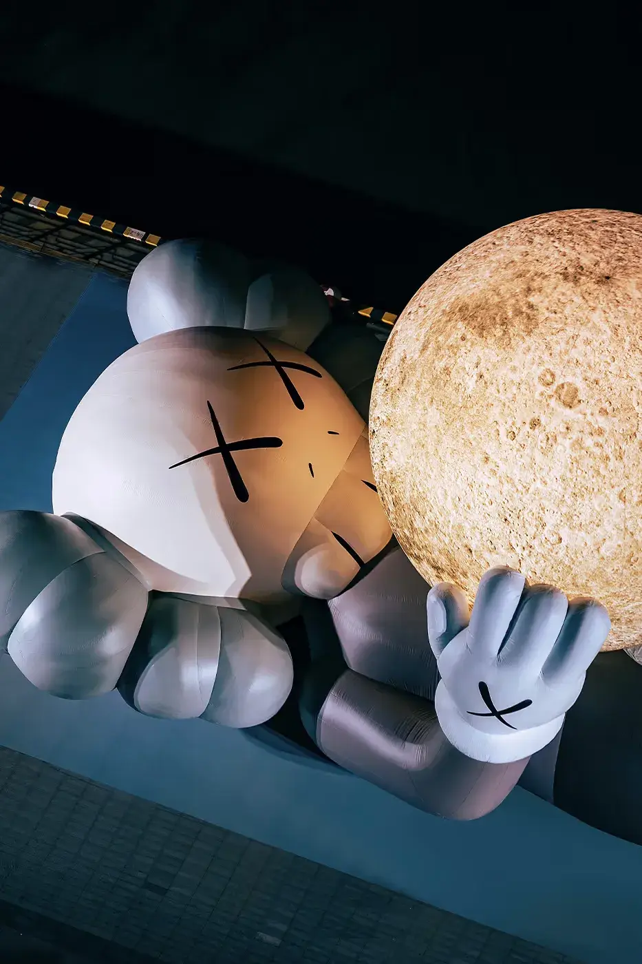 KAWS:HOLIDAY Shanghai installation featuring COMPANION holding glowing moon at North Bund, with details on limited edition vinyl figures and merchandise (image 4 of 4)