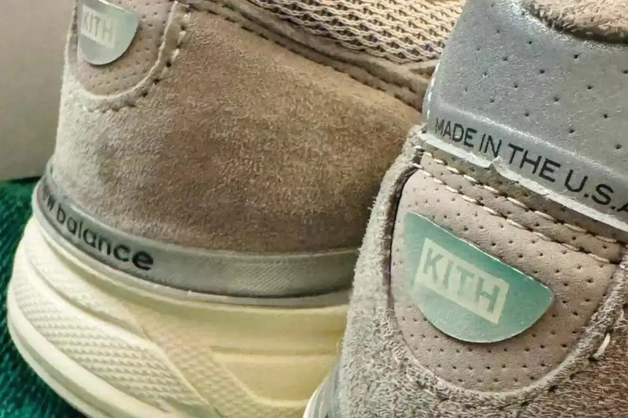 KITH x New Balance 990v4 sneaker in Grey and Cream colorway. Side view showing soft brown upper with grey 'N' logo, distinct KITH branding on heel, and off-white sole. A blend of classic design and contemporary streetwear aesthetics (image 2 of 2)