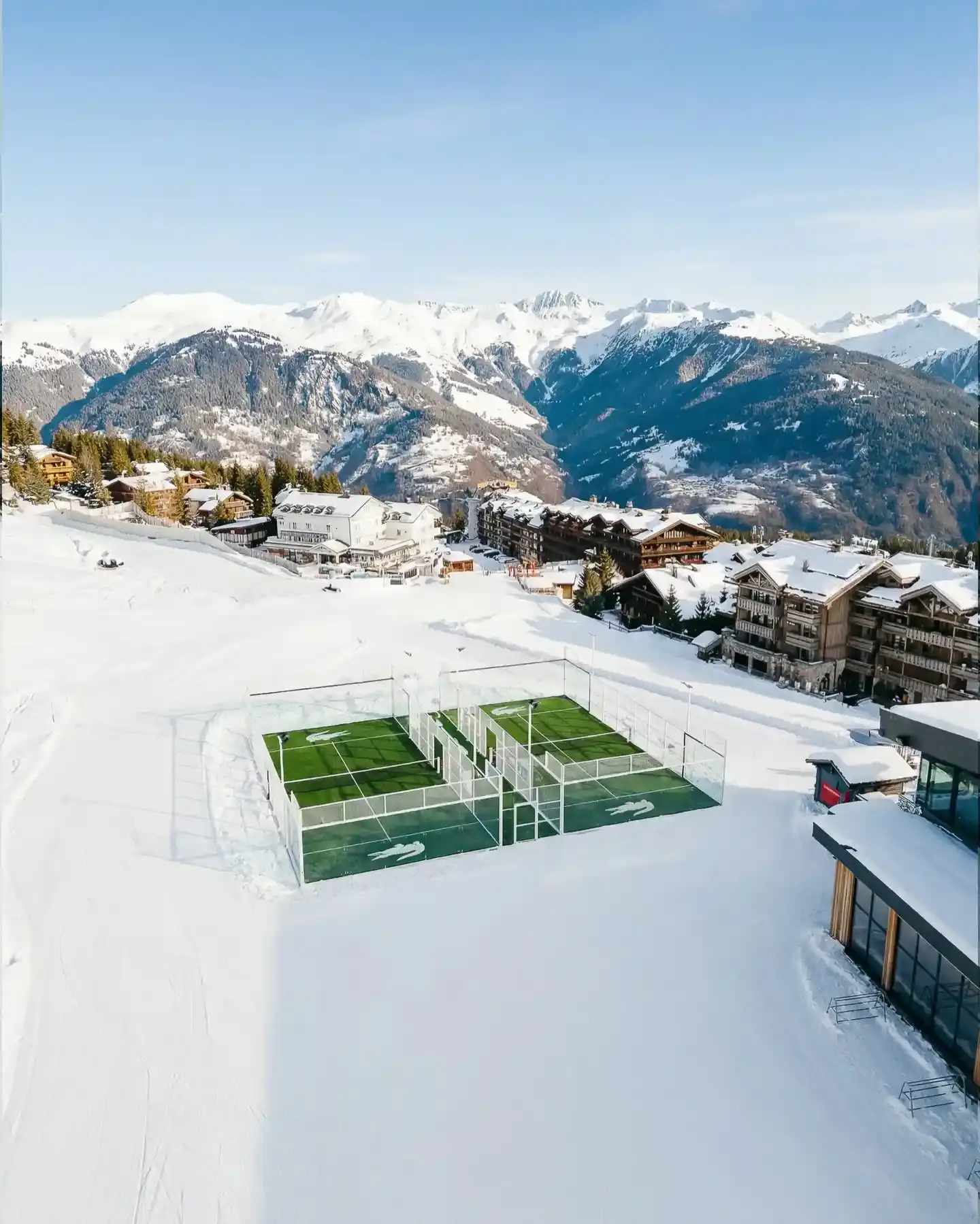 Two green padel courts installed by Lacoste at the base of Émile Allais slalom stadium in Courchevel, French Alps, with snow-covered mountains in the background and INEOS Club House visible nearby.