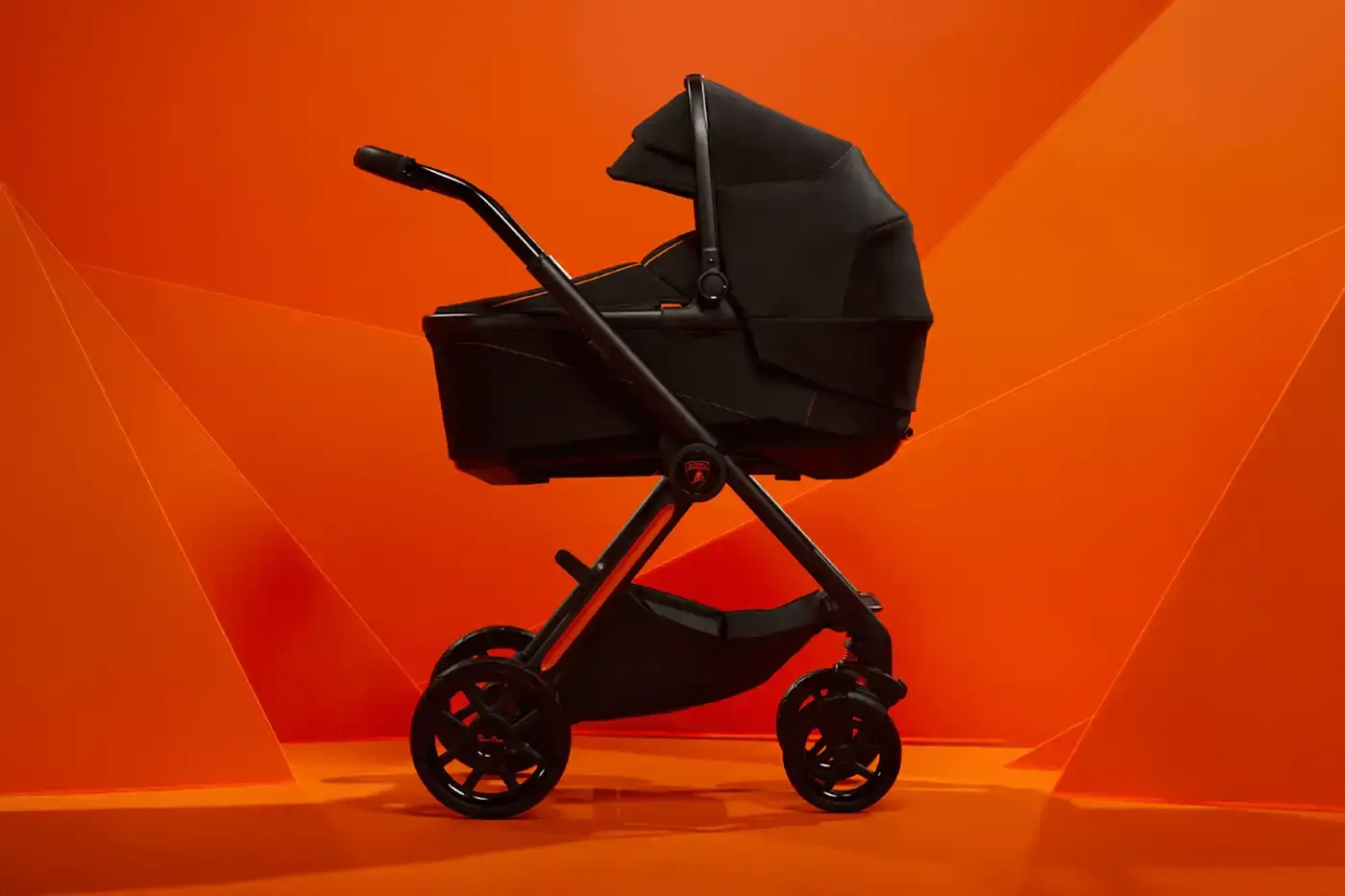 Silver Cross/Automobili Lamborghini Black and orange Lamborghini x Silver Cross Reef AL Arancio baby stroller with full suspension wheels, leather accents, and automotive-inspired handlebars shown against neutral background.